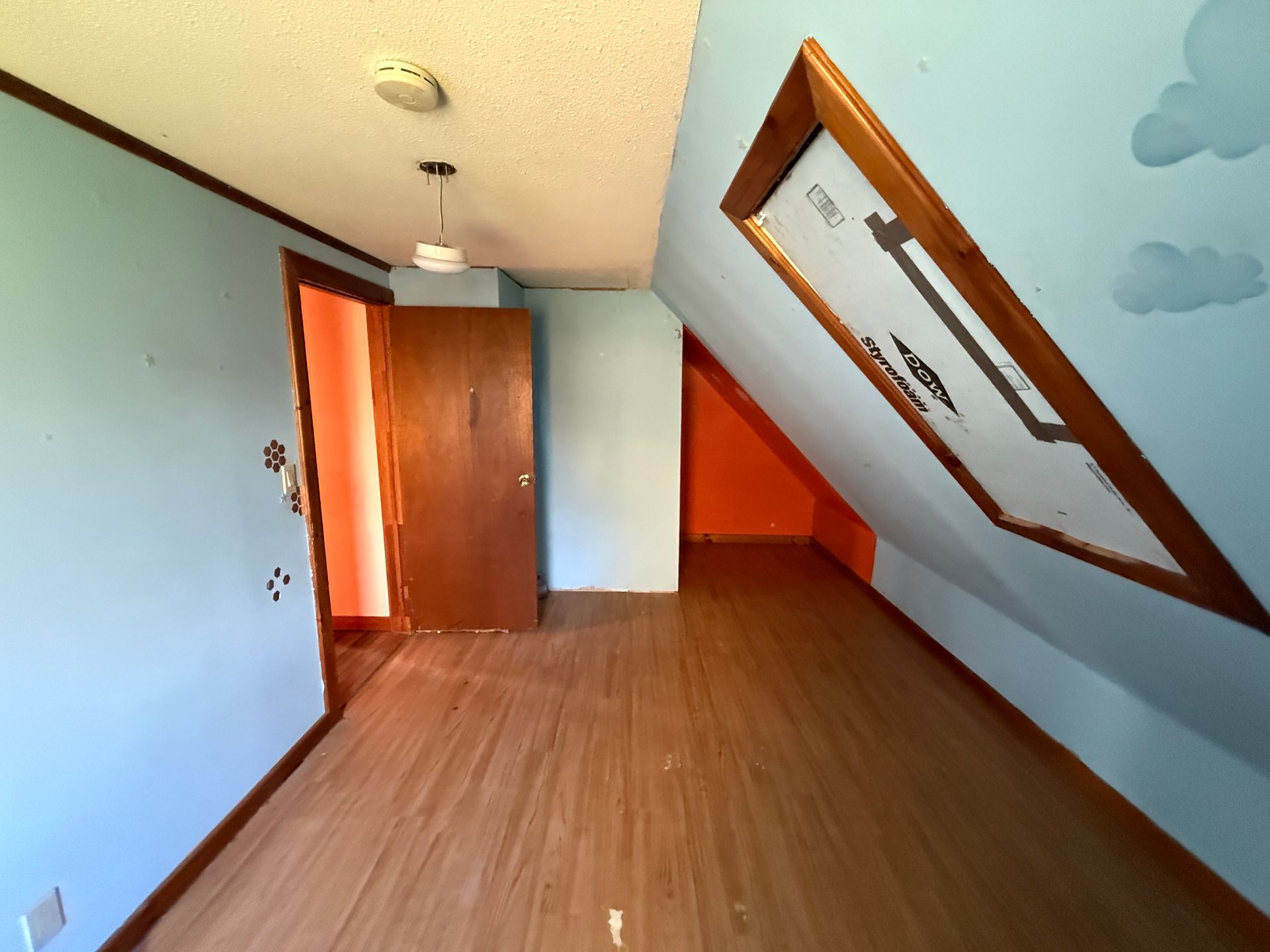 Empty attic room with slanted white ceiling, wood floor, and open door.