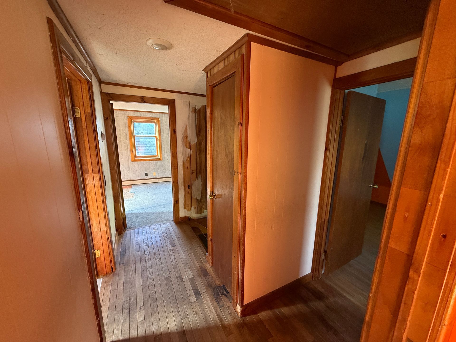 Narrow hallway with wood trim, peach walls, and doorways leading to a room with a blue wall and window.