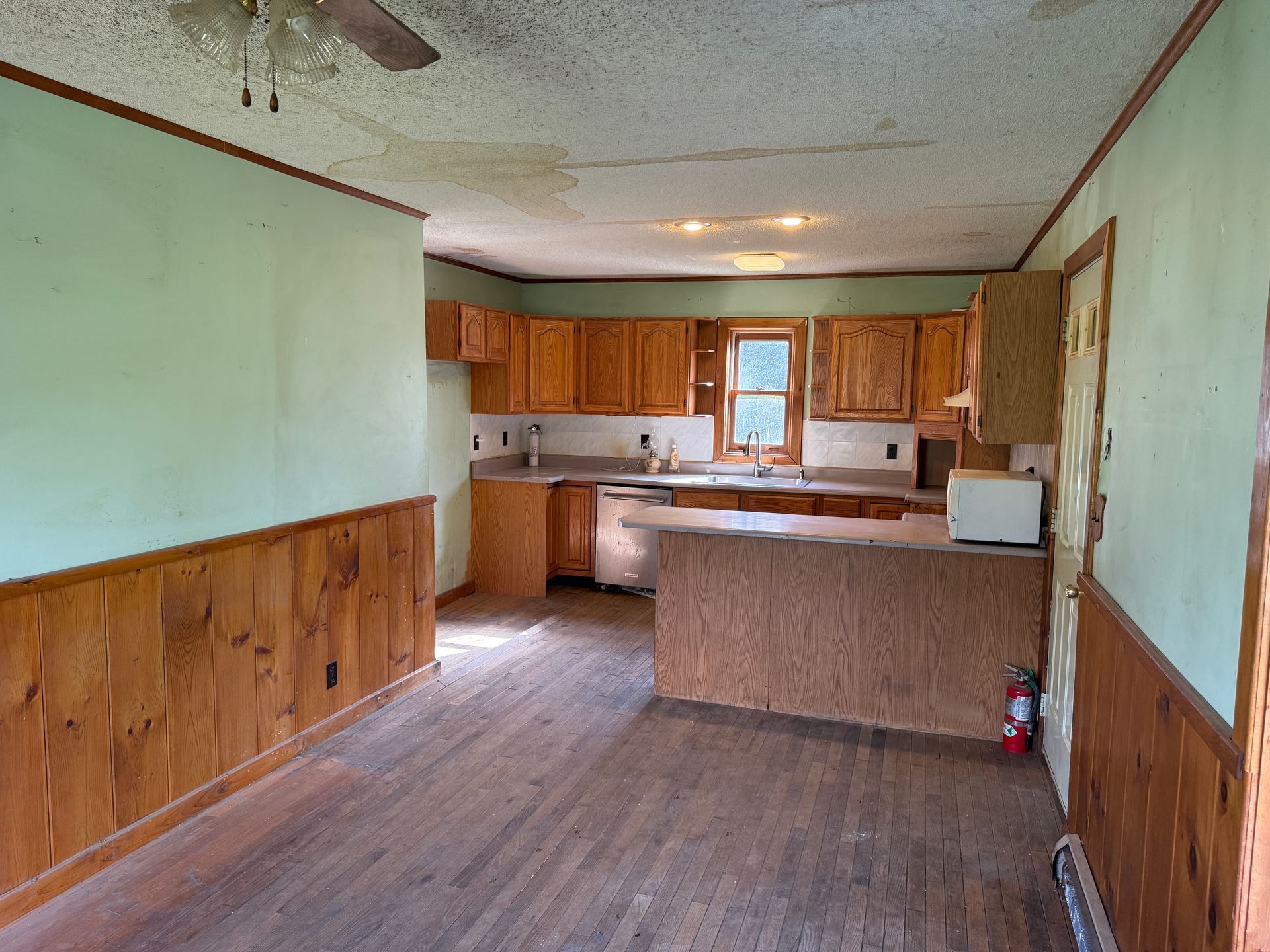 Empty kitchen and dining area with wood cabinets, green walls, and a floor.