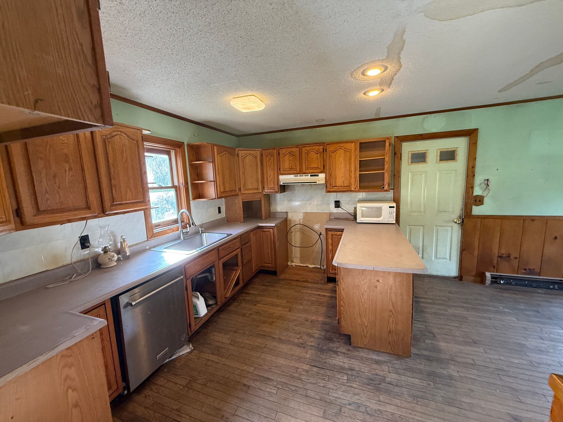 Bright kitchen with wood cabinets, white appliances, and a small center island on a wood floor.