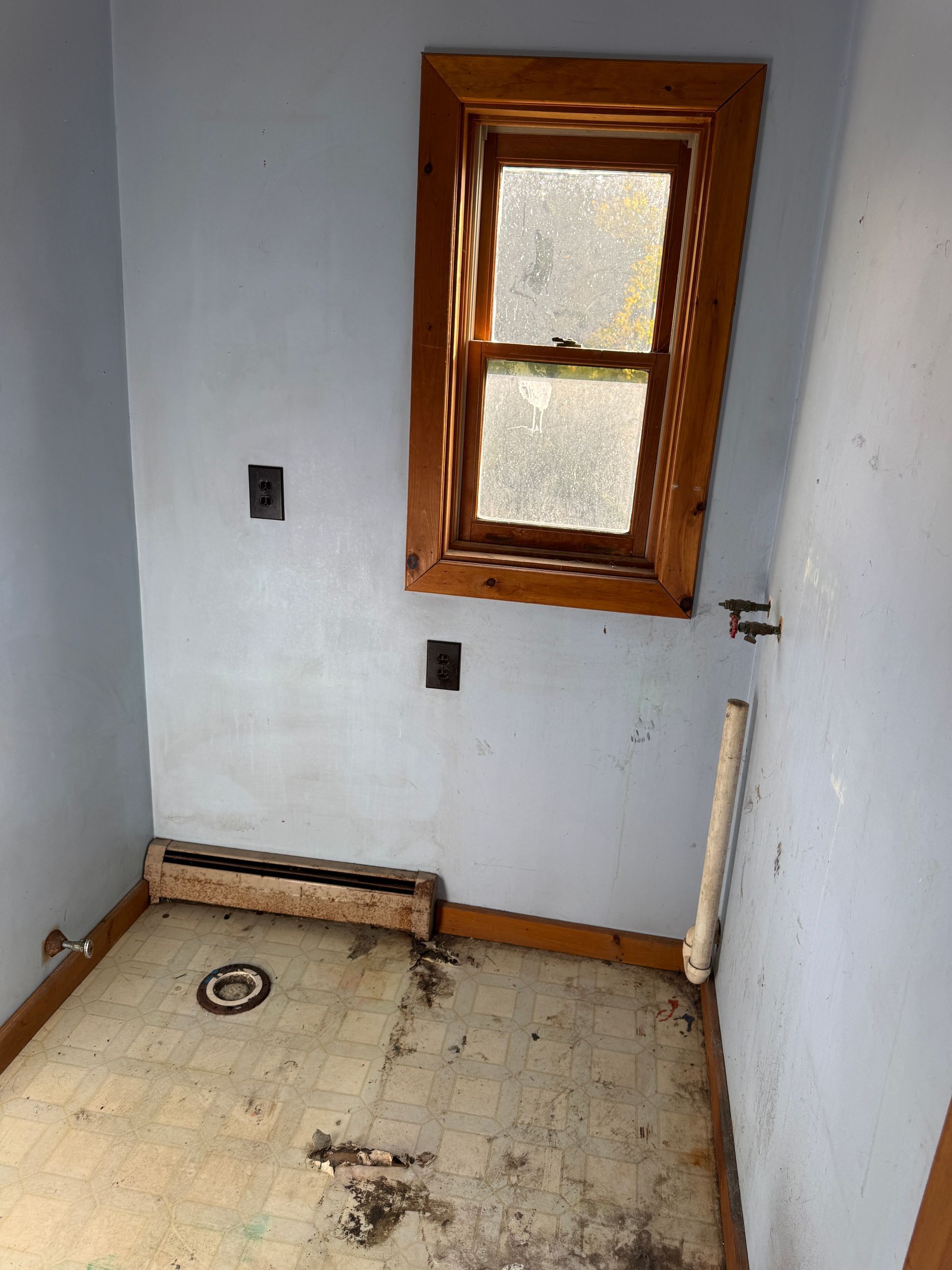 Small room with white walls, bare floor, a small wood-framed window