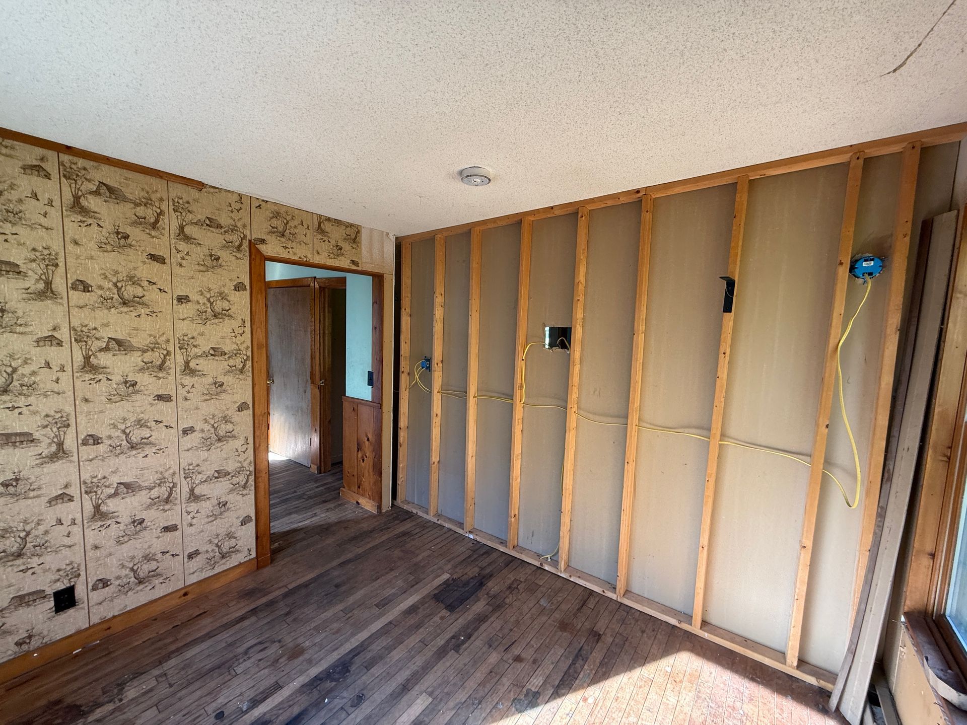 Empty room under renovation with exposed wall studs, wallpaper, and wood flooring