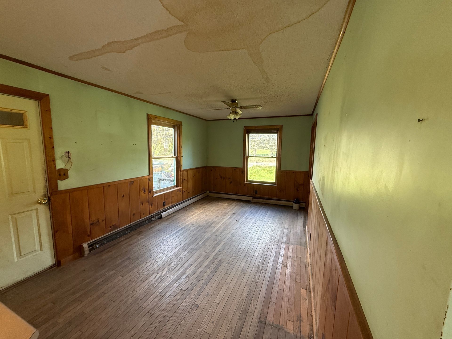 Empty room with wood floors, green walls, and two windows letting in daylight.