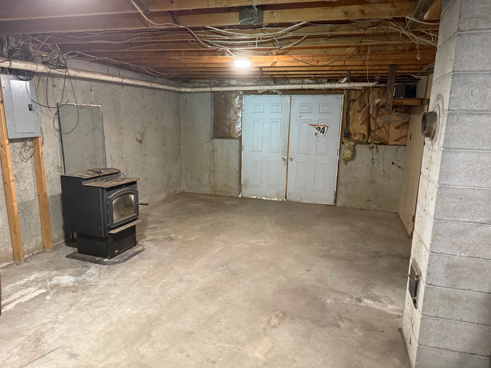 basement with concrete walls, exposed ceiling joists, and a wood stove on the left.