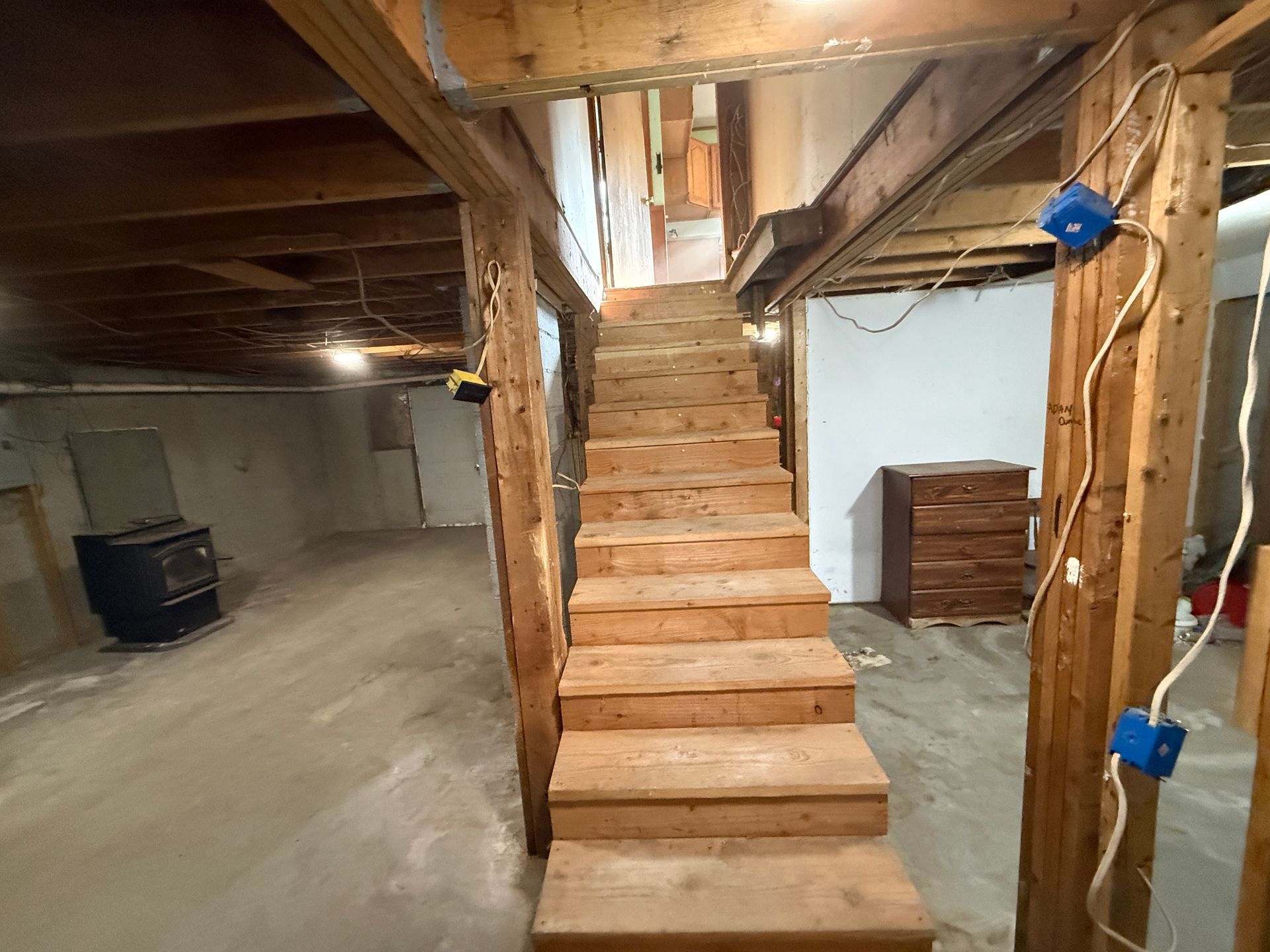 Basement with unfinished wooden stairs leading to an upper level, exposed beams, and a laundry area