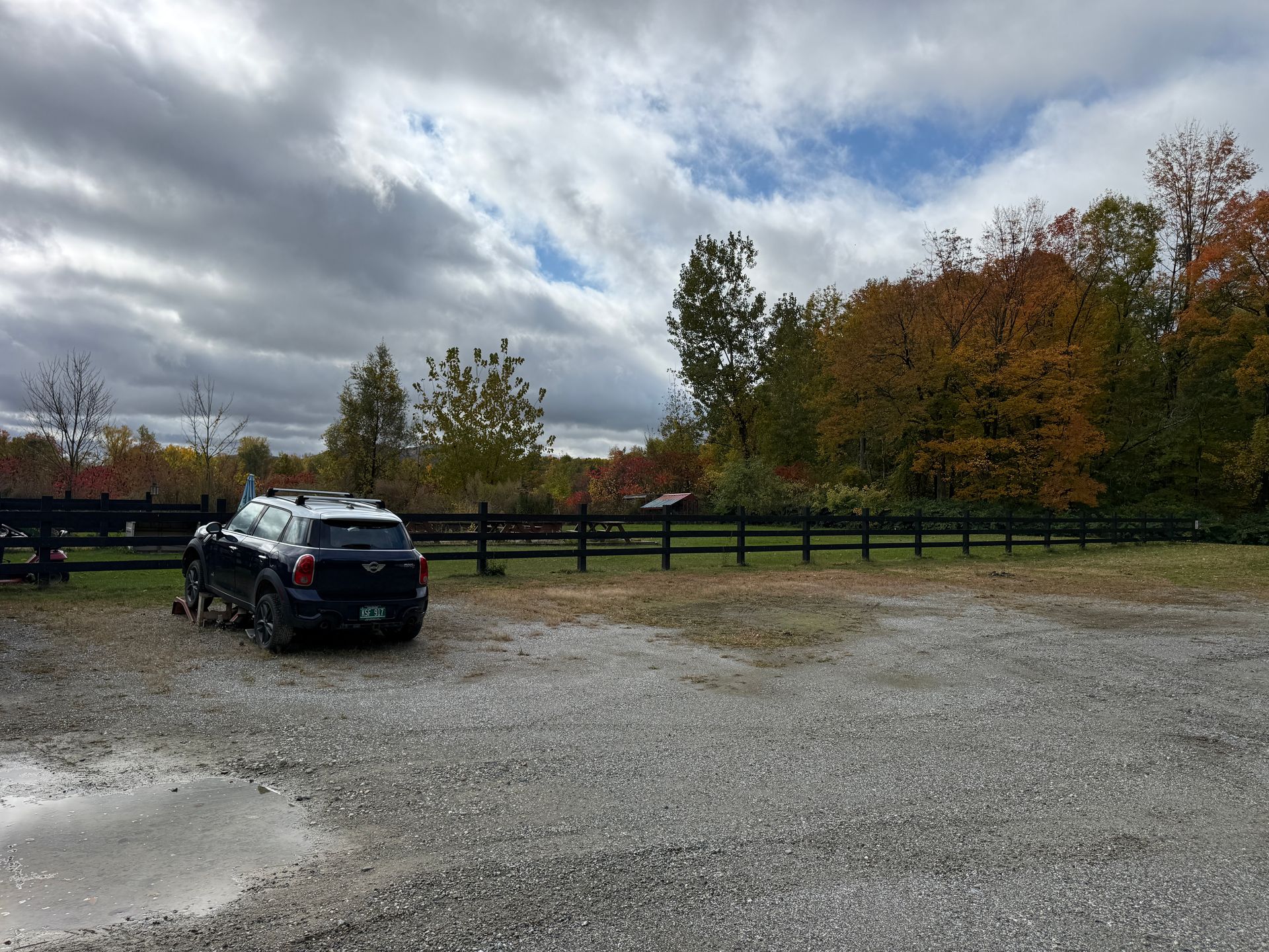 Black SUV parked on a gravel lot beside a wooden fence under a cloudy autumn sky.