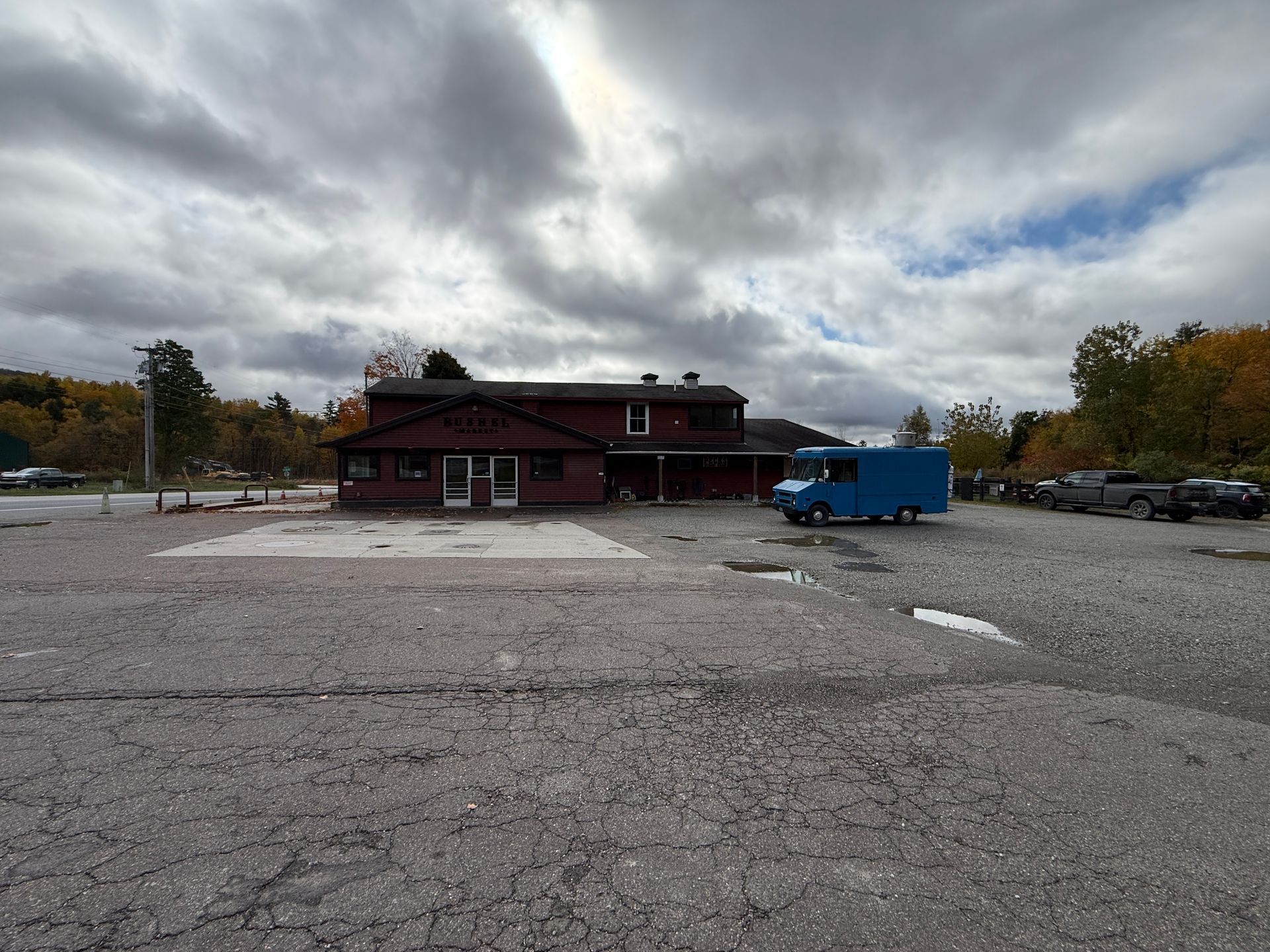 Rural parking lot with a red building, blue trailer, and cloudy sky in autumn.