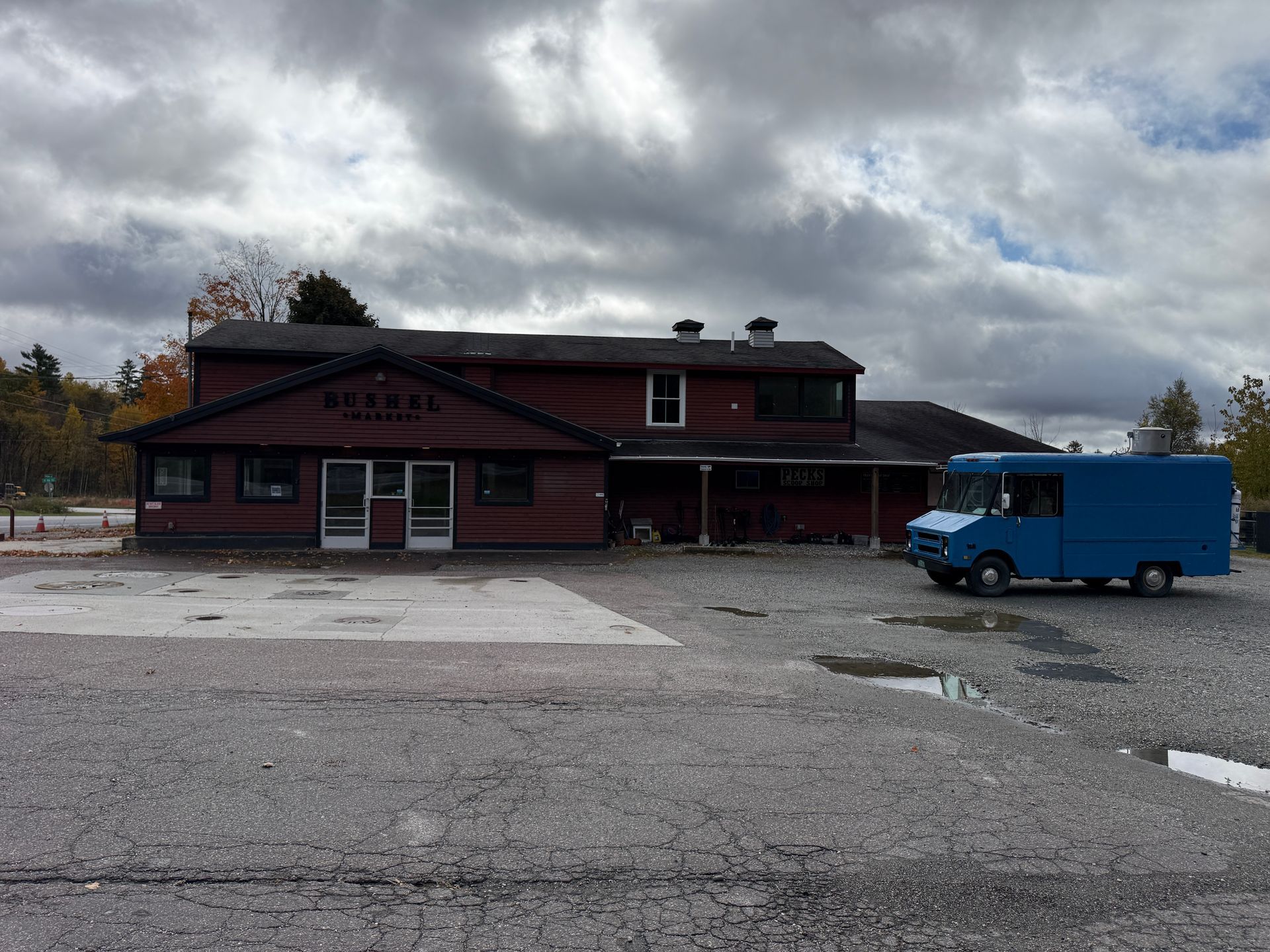 Red building under cloudy sky with a blue delivery truck in a gravel lot