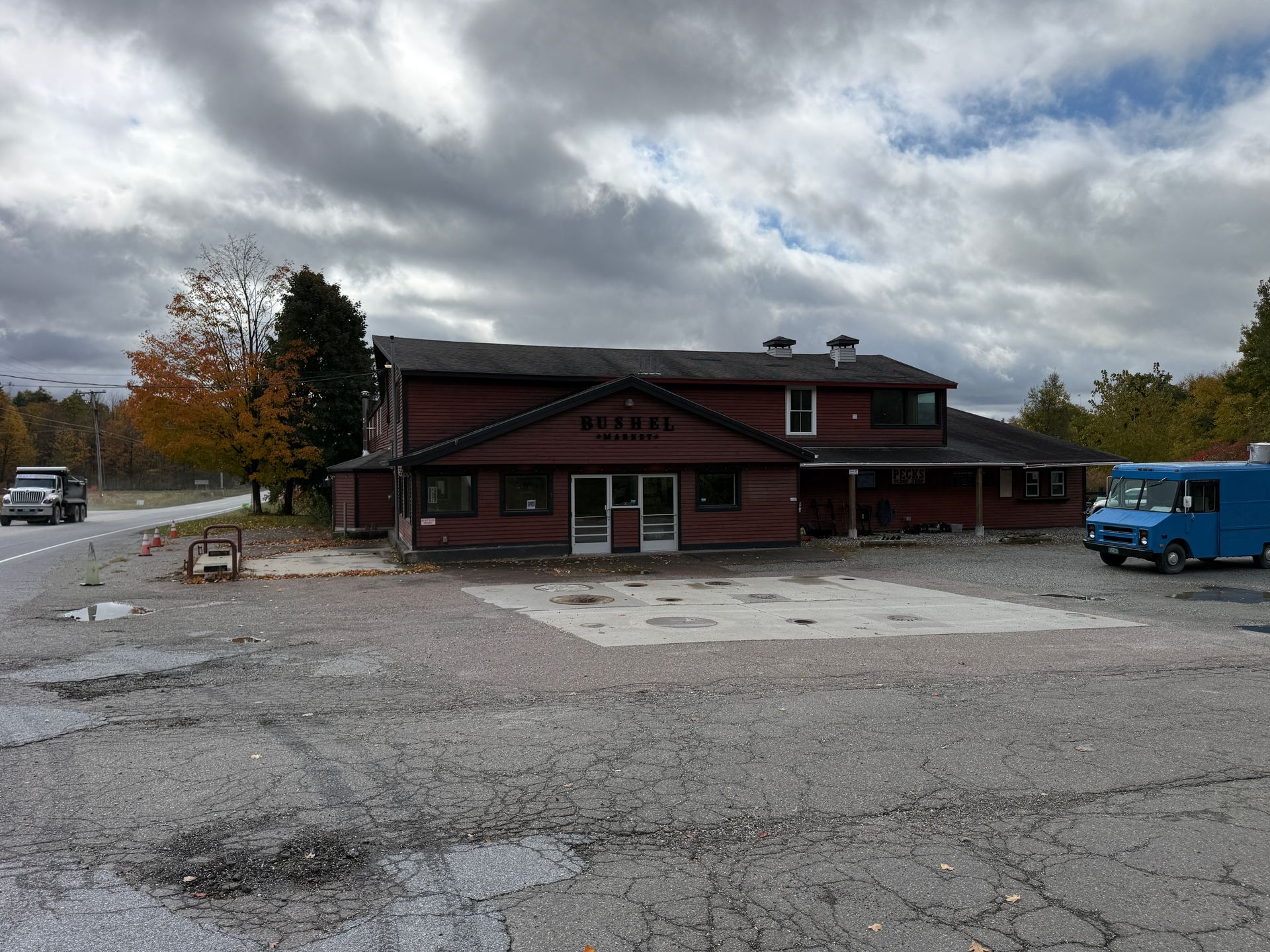 Rustic red building with a cloudy sky, empty lot, and blue truck parked on the right.