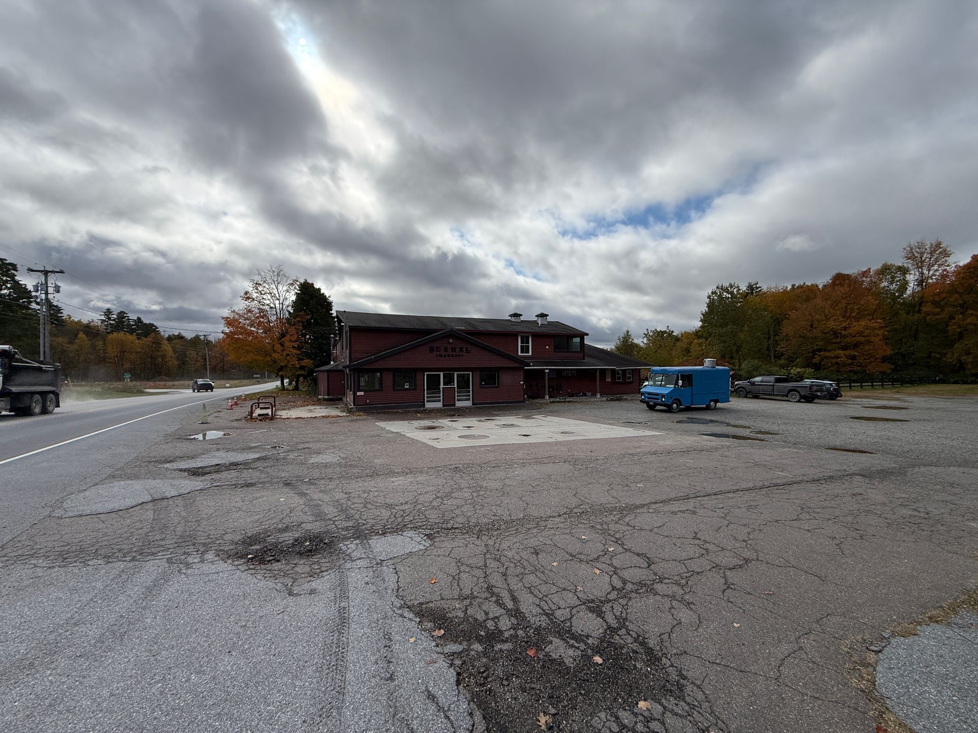 Empty parking lot with a red building, blue truck, and cloudy autumn sky