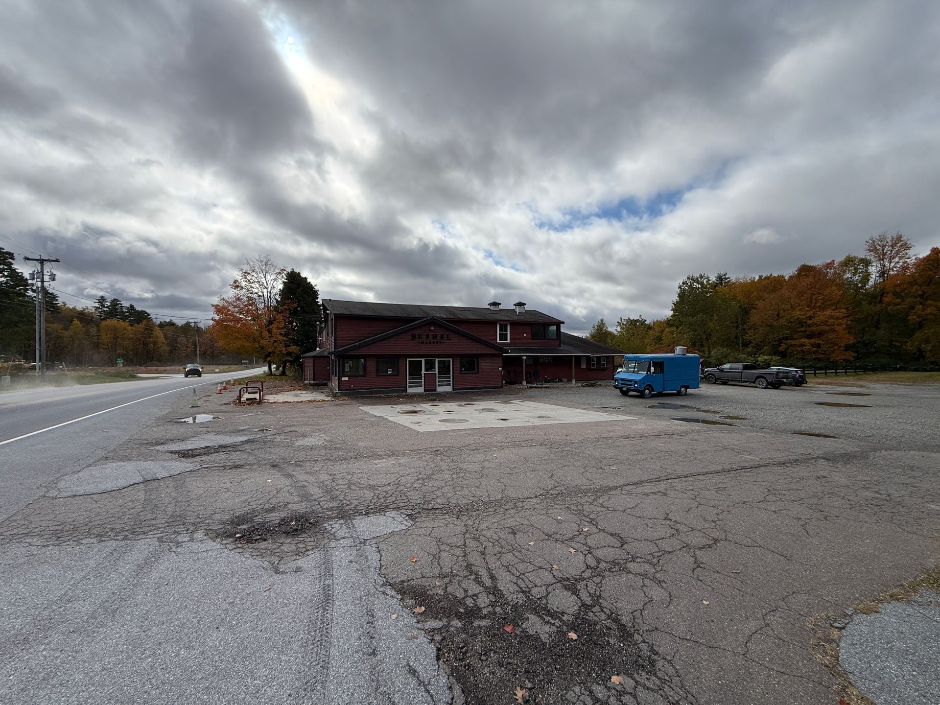 Wide gravel parking lot with a red building and a blue van under a cloudy autumn sky