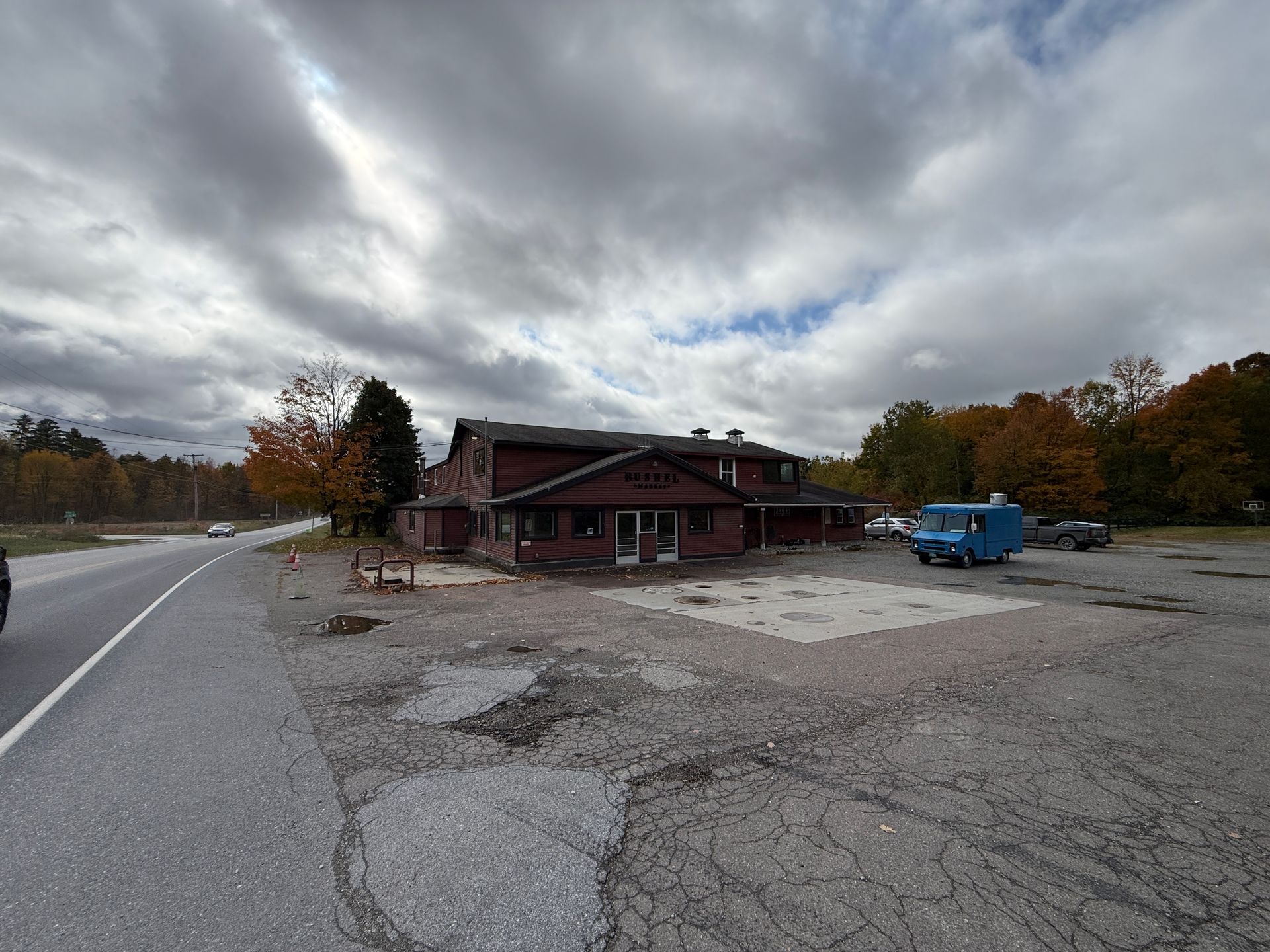 Rural roadside building with gravel lot, parked blue truck, and cloudy autumn sky
