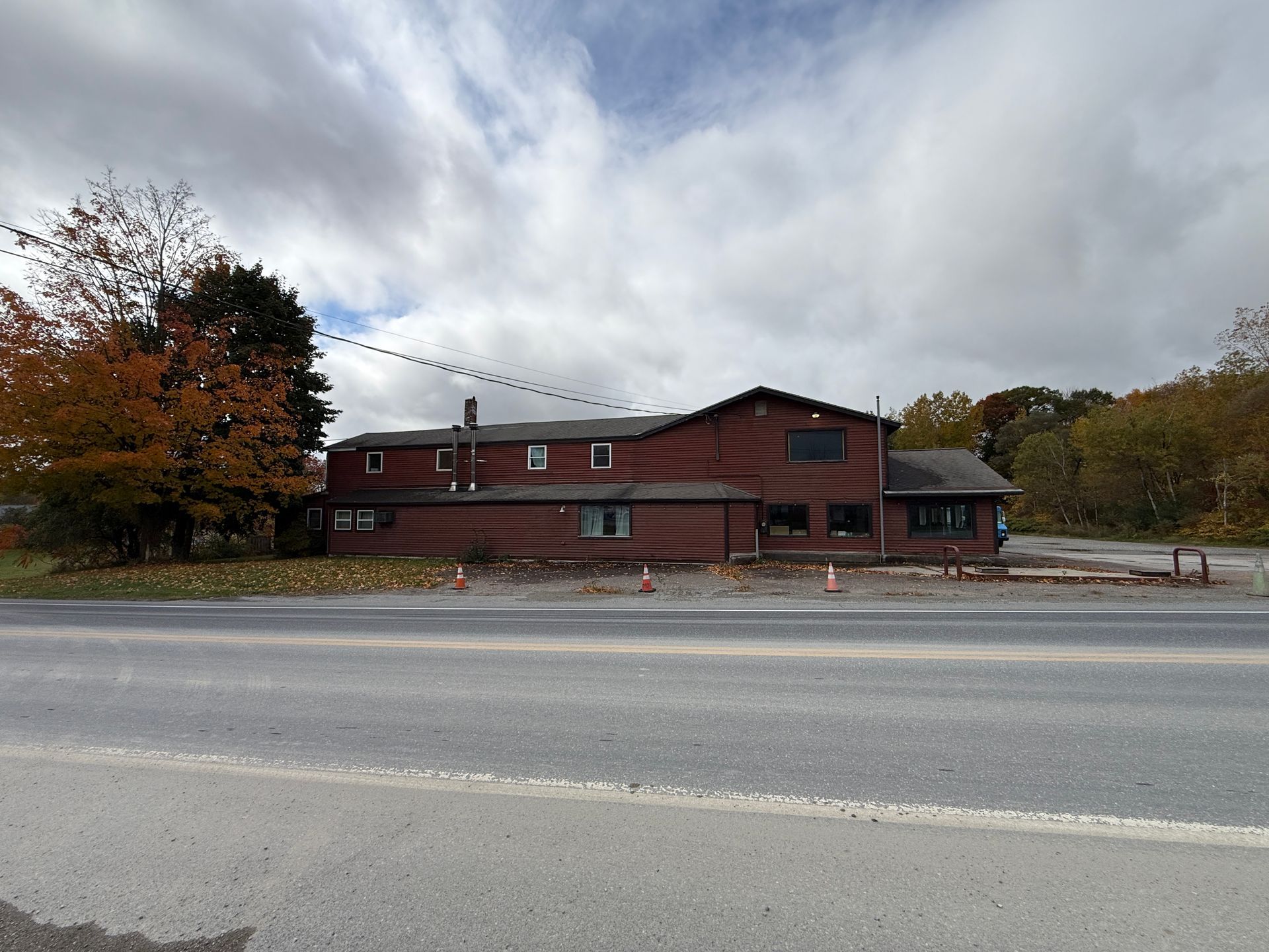 Red brick building by a roadside under cloudy skies, with autumn trees nearby