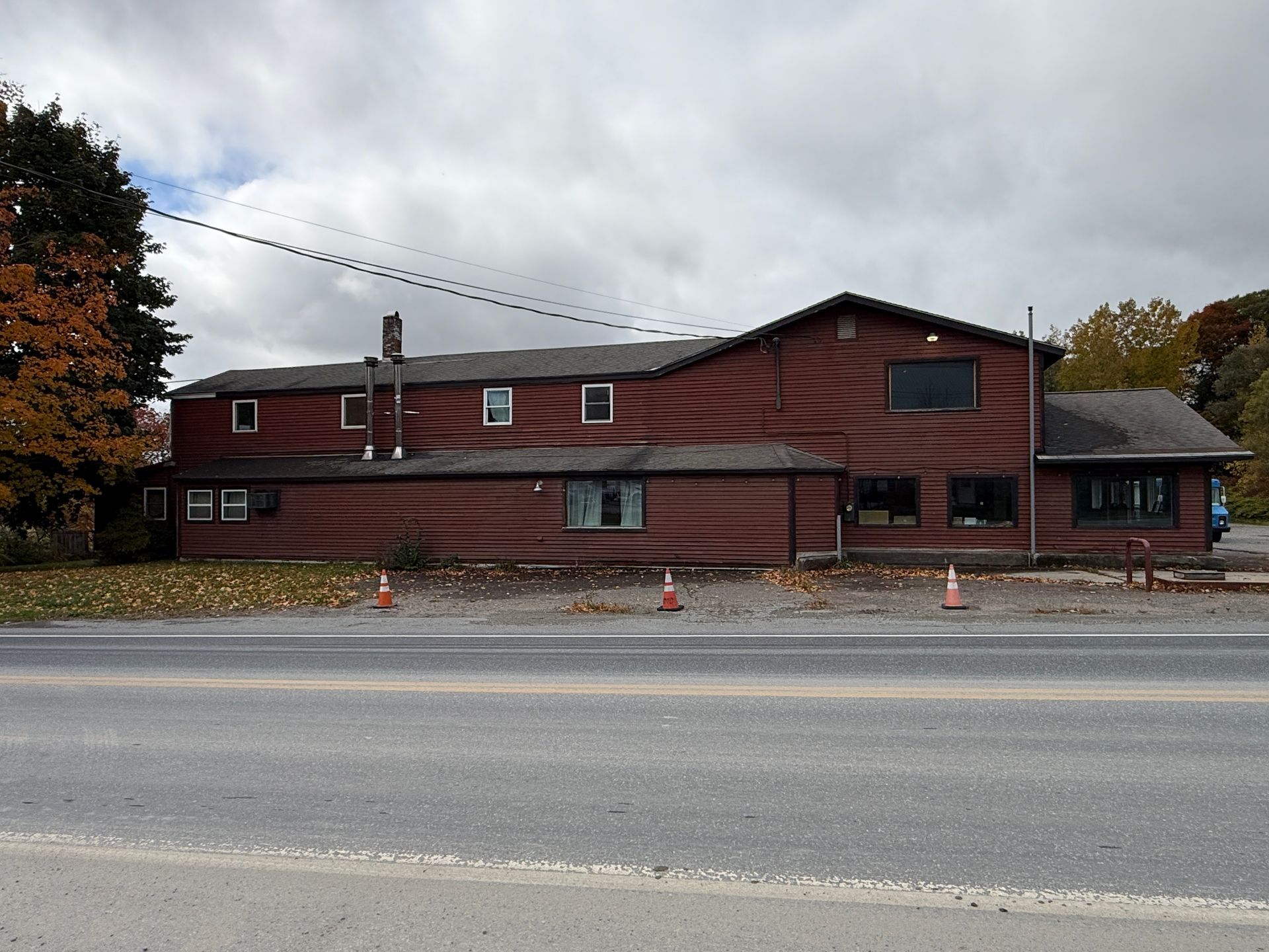 Red wooden roadside building with a covered porch and parked construction cones in front