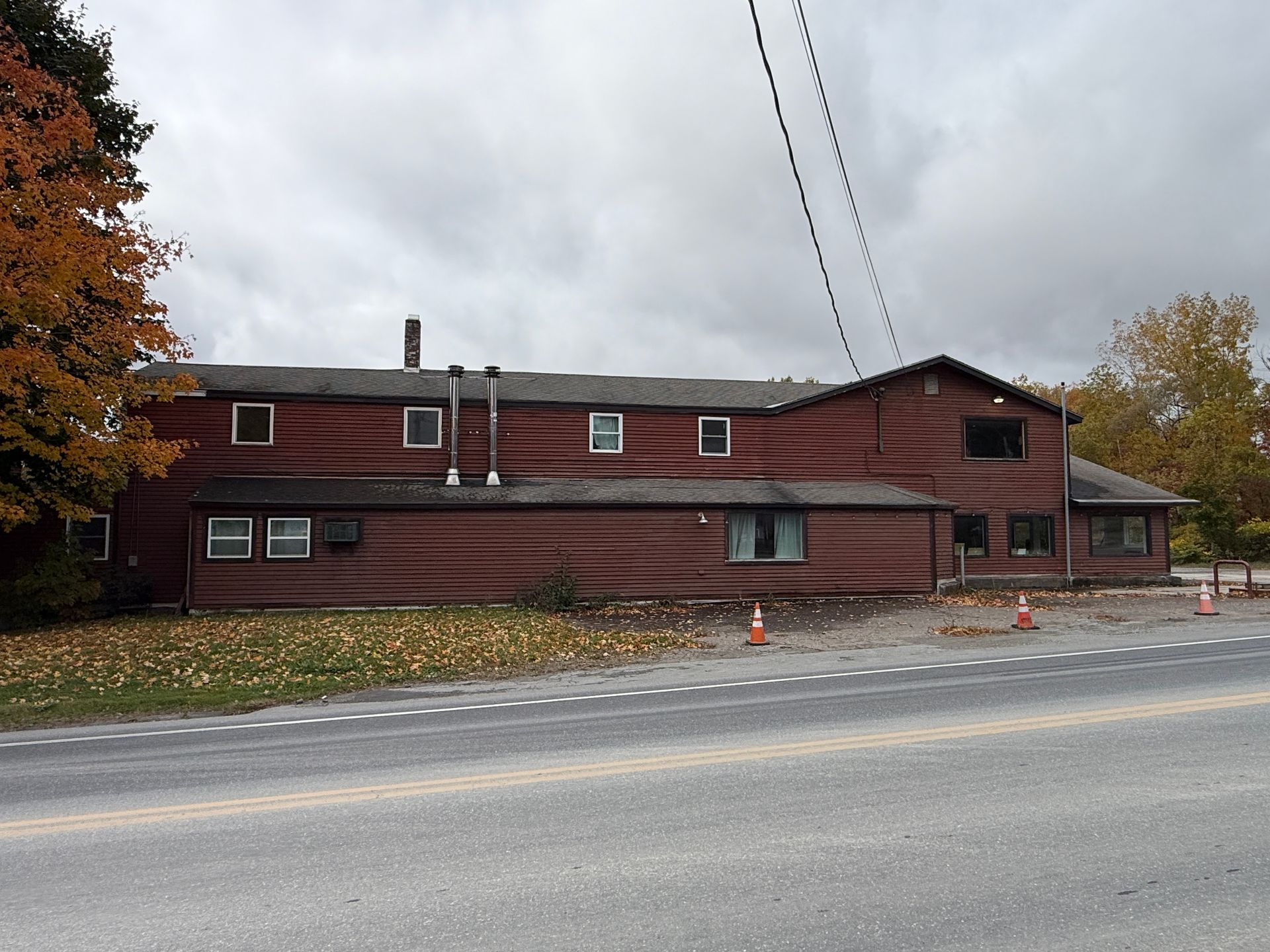 Brown wooden building beside a road under cloudy skies, with orange cones near the curb