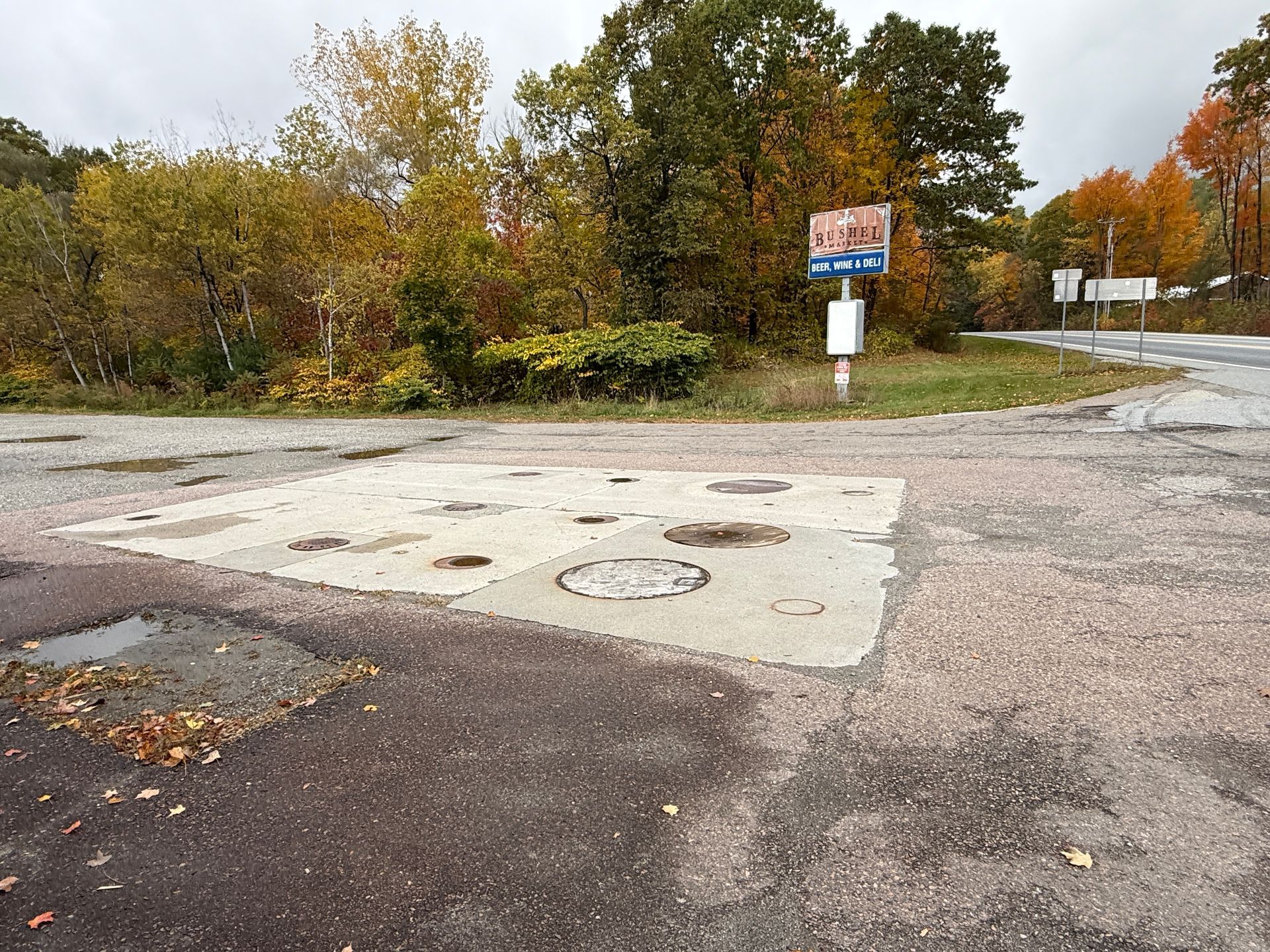 A parking lot beside a wooded roadside with a sign and autumn trees.