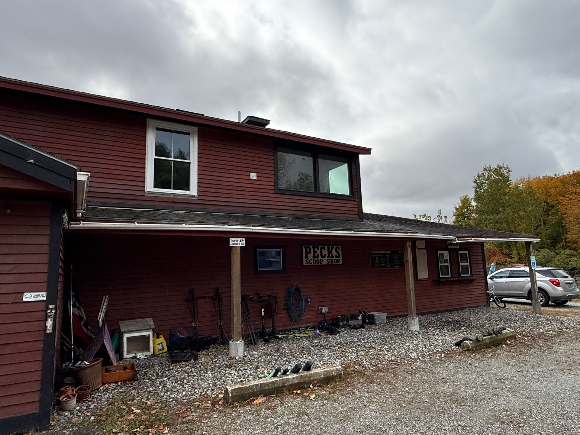 Two-story red house with covered porch and gravel driveway under a cloudy sky