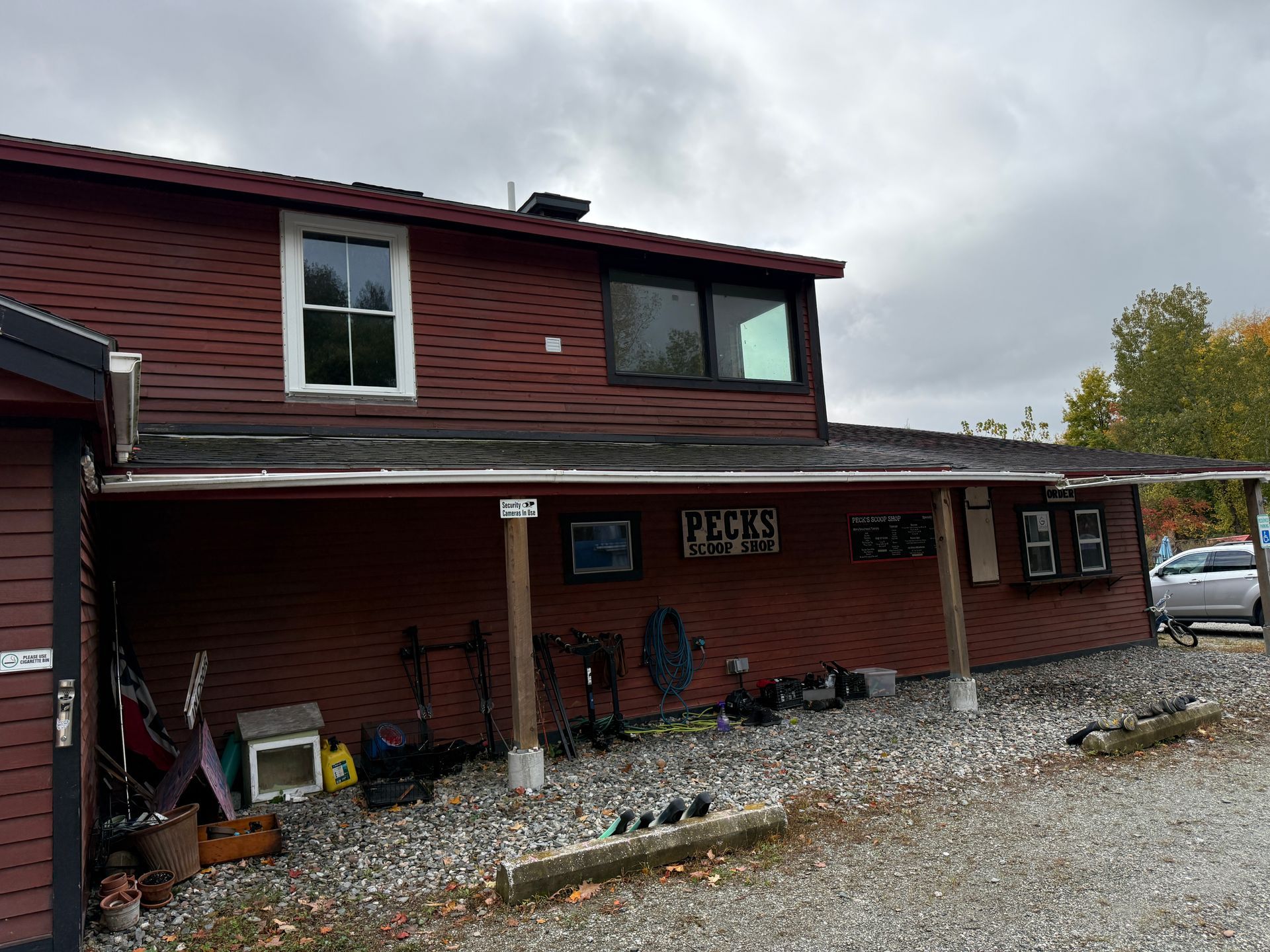 Red two-story house with porch and gravel yard under a cloudy sky