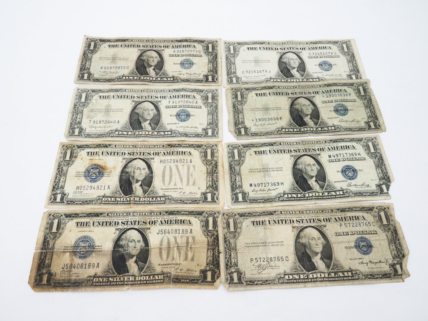 Eight worn one-dollar bills arranged on a white surface, featuring George Washington's portrait.