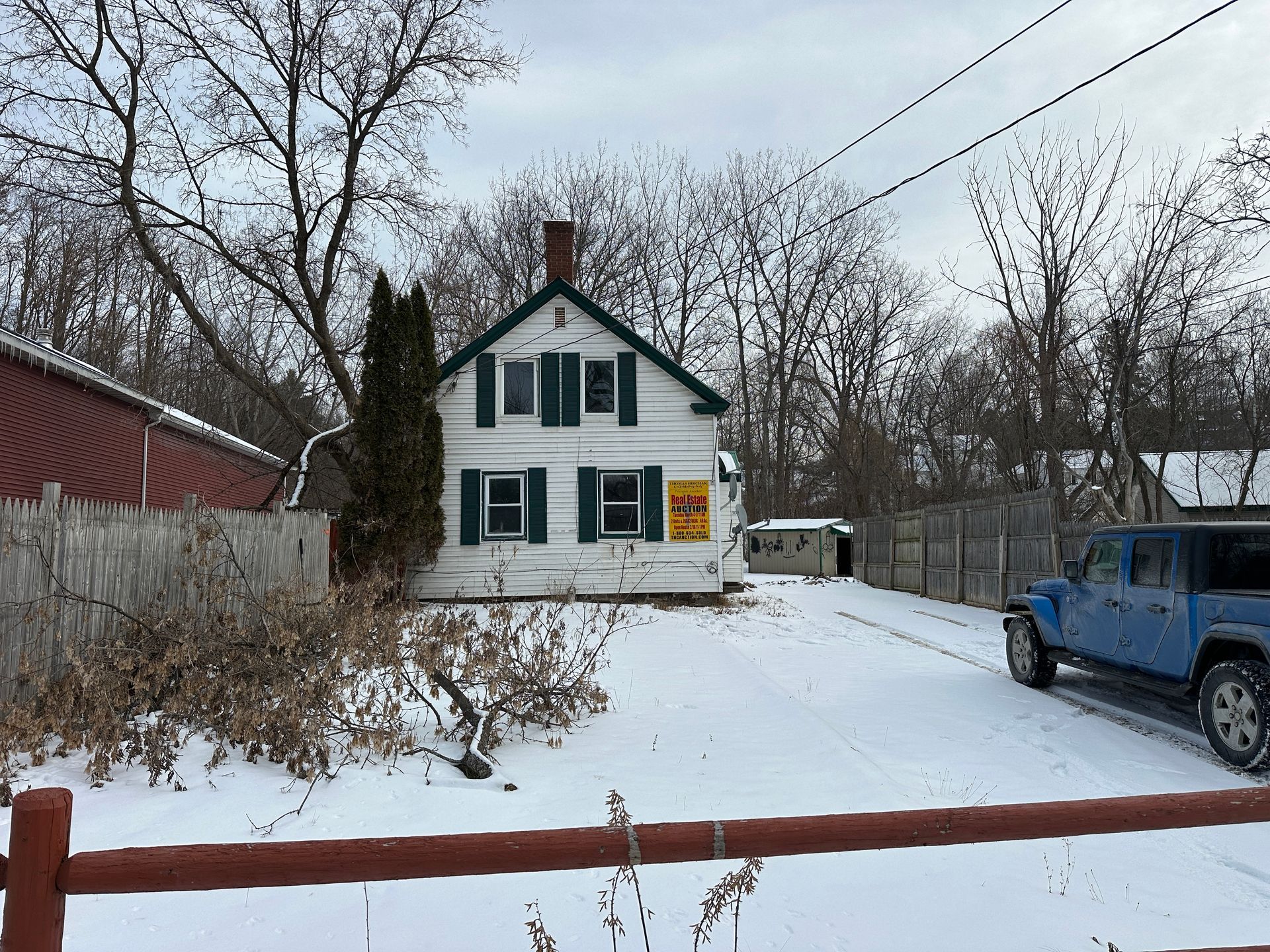 White house with green shutters, snow-covered yard, bare trees, red barn, blue truck.