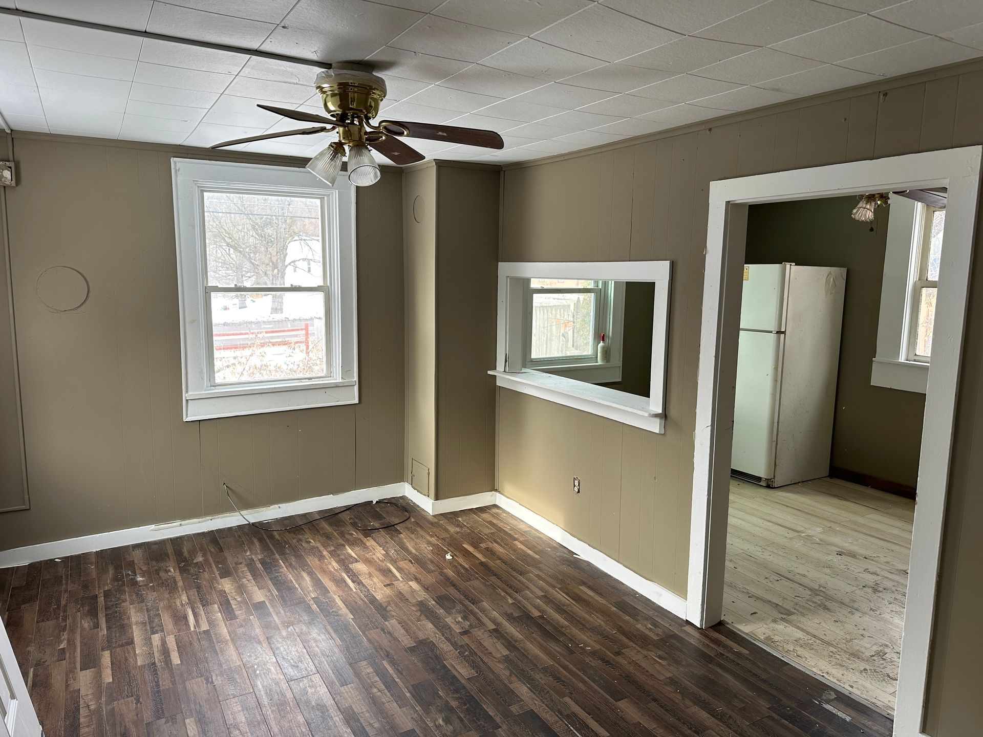 Empty room with dark wood-look floor, tan walls, white trim, and a ceiling fan.