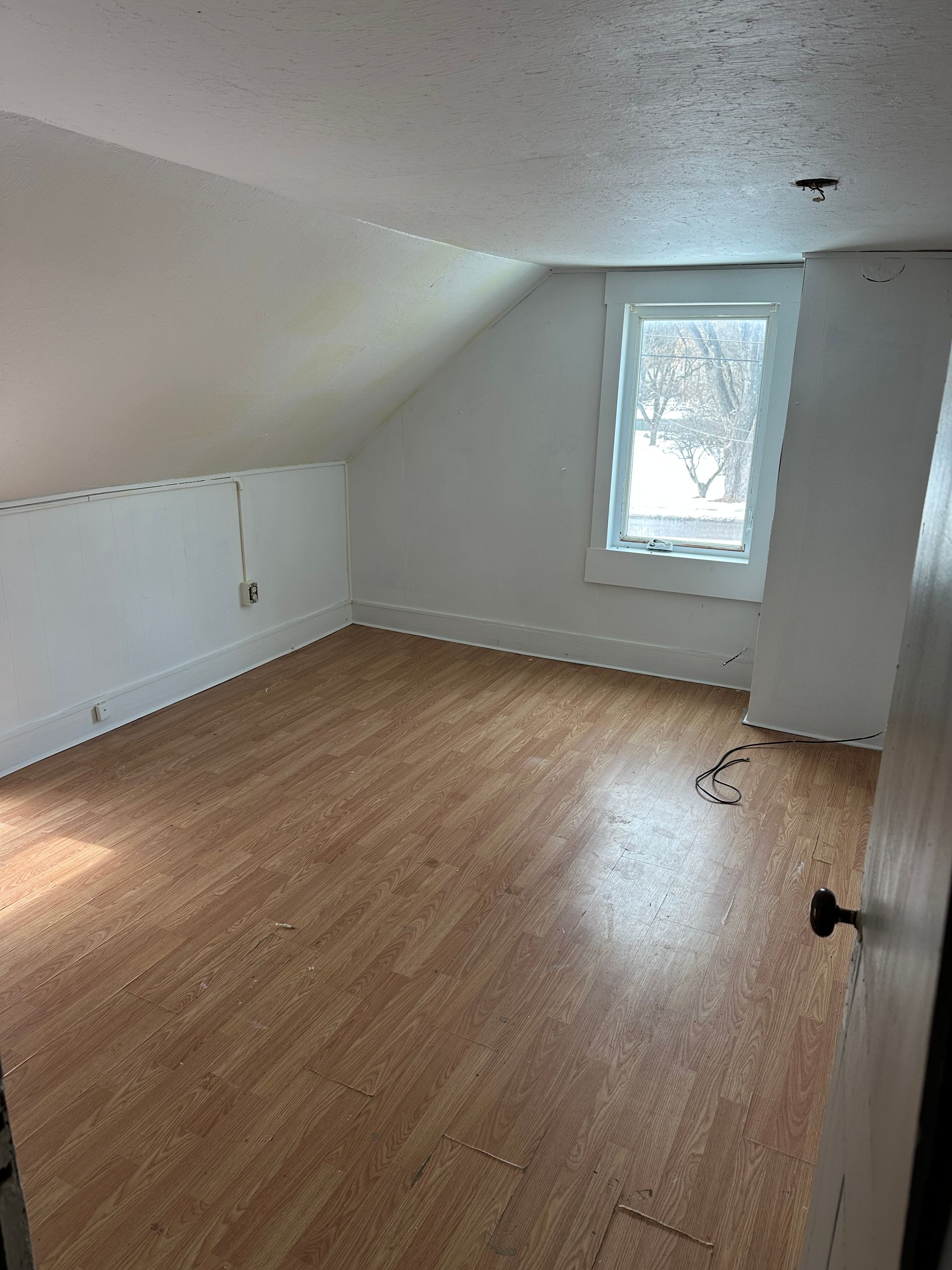 Small room with slanted ceiling, window, and wood-grain flooring.