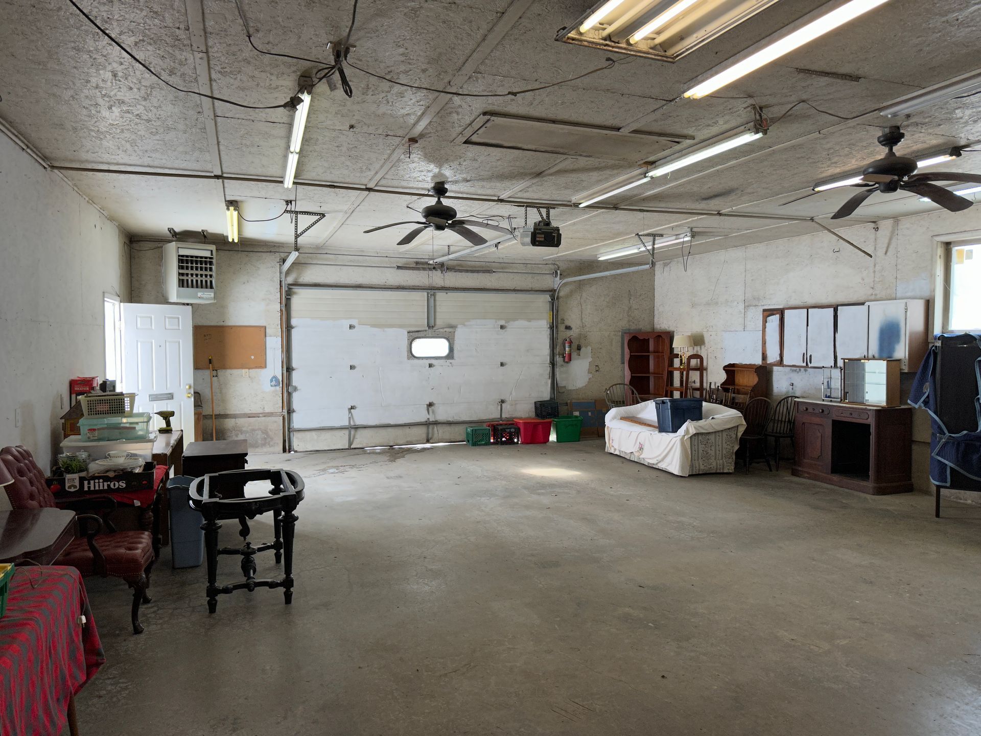 Garage with concrete floor and open garage door; contains furniture, boxes, and ceiling fans.