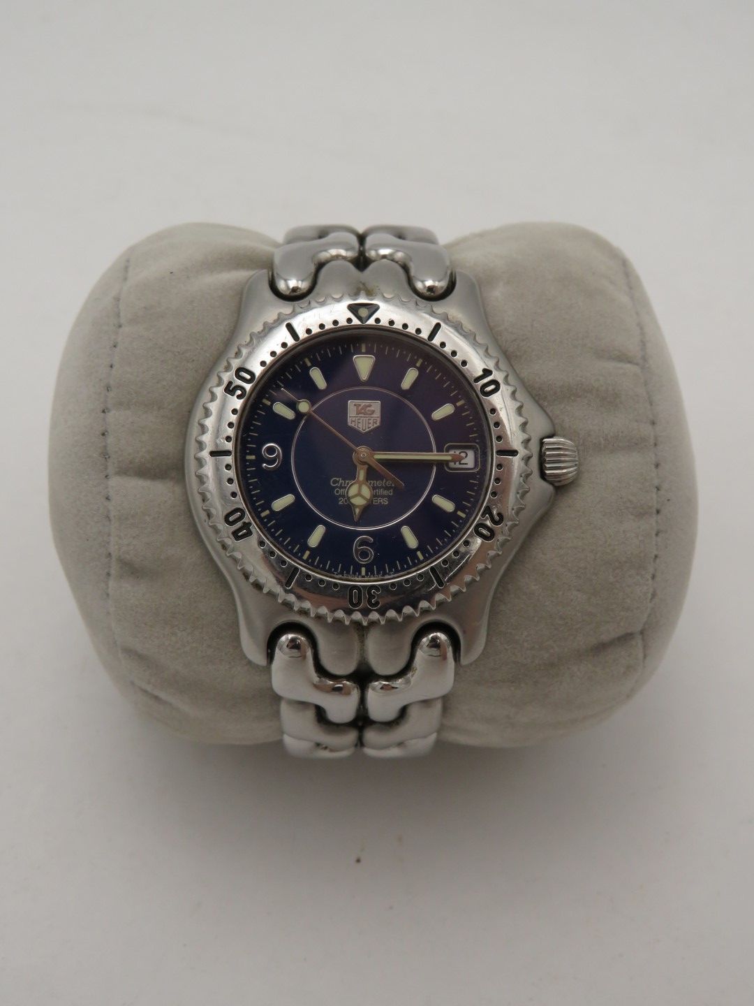 Silver wristwatch with a blue face on a grey cushion.