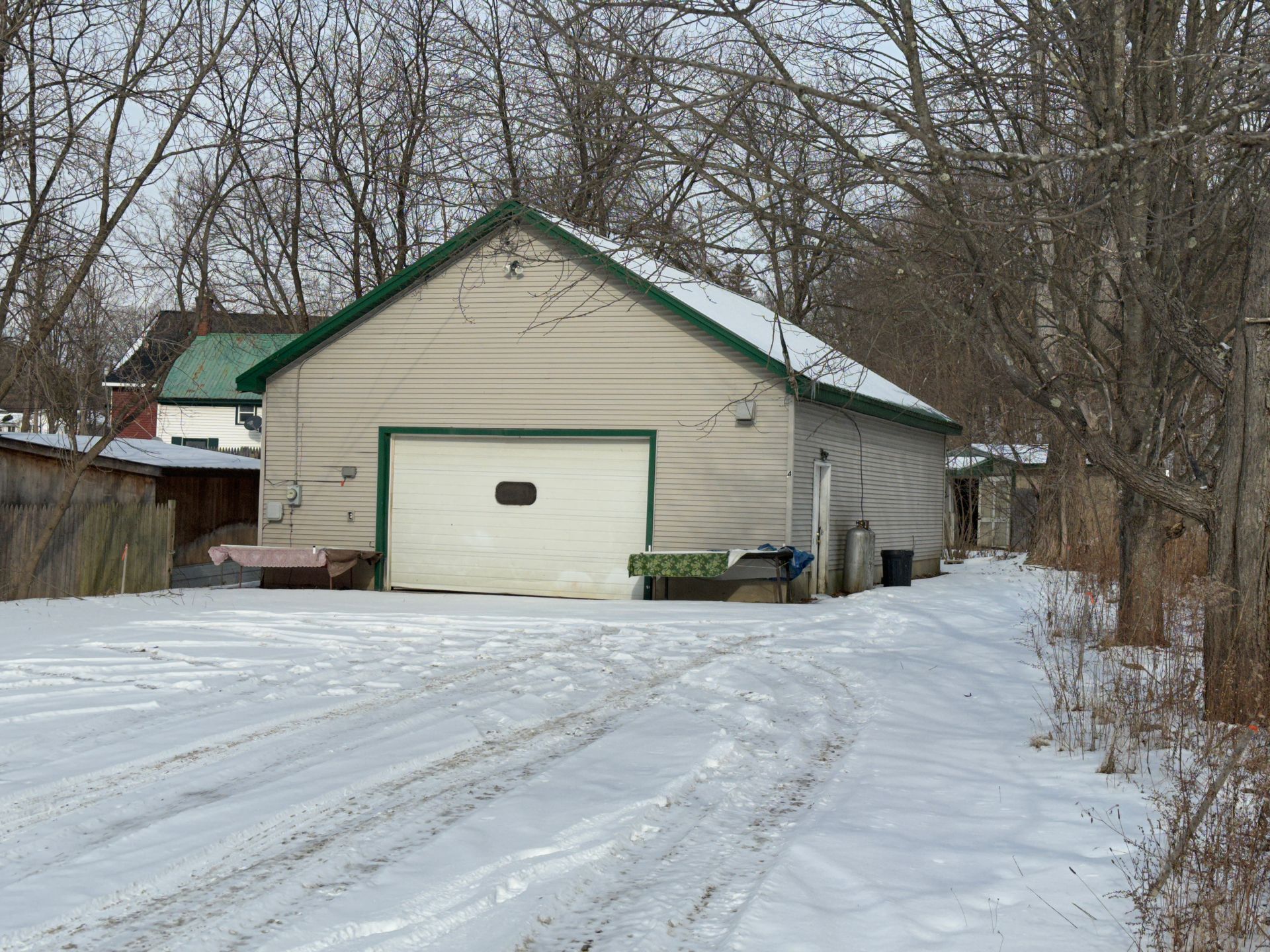 Snowy driveway leading to a light-colored garage with green trim.