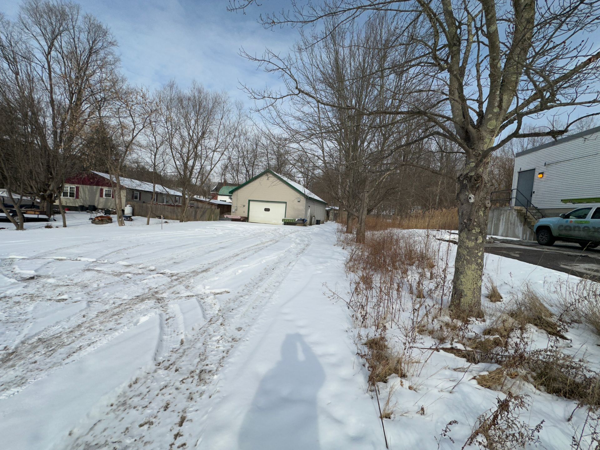 Snowy outdoor scene. A building with an open garage faces a snow-covered parking area. A semi truck is on the right.