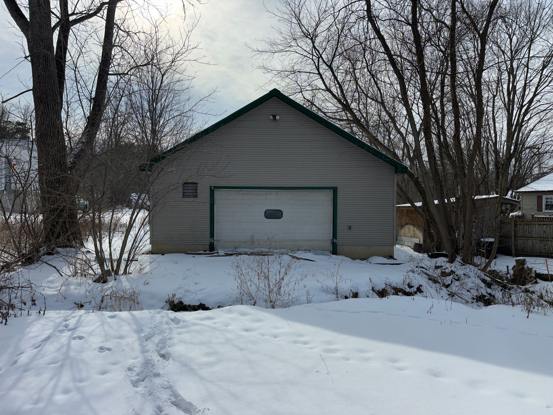 Snow-covered landscape with a gray garage featuring a white overhead door and green trim.
