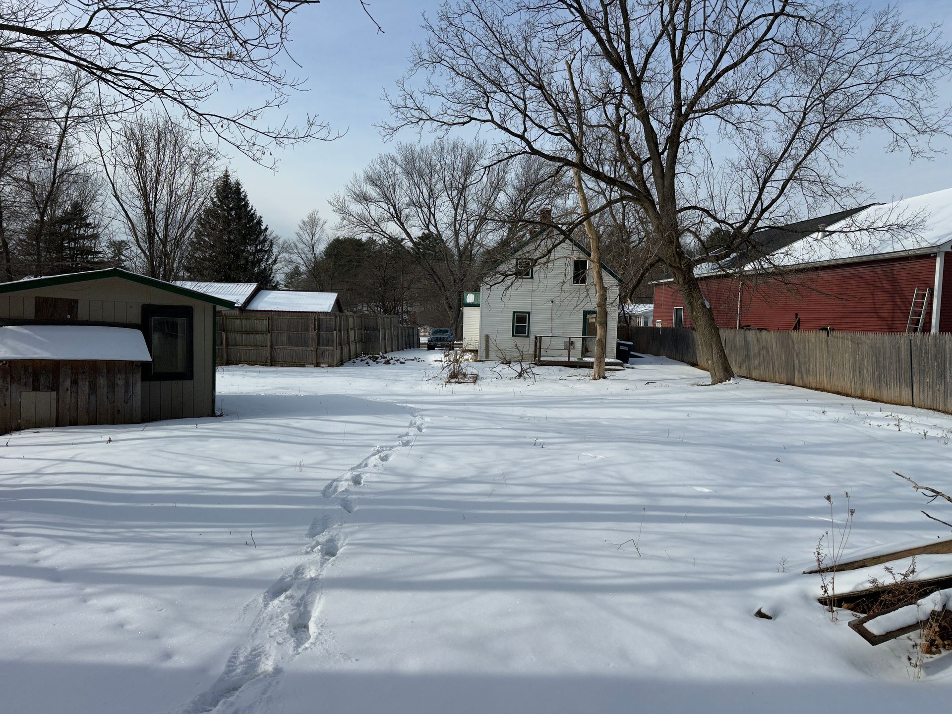 Snowy backyard scene with tracks leading to a house, shed on left, red barn on right.