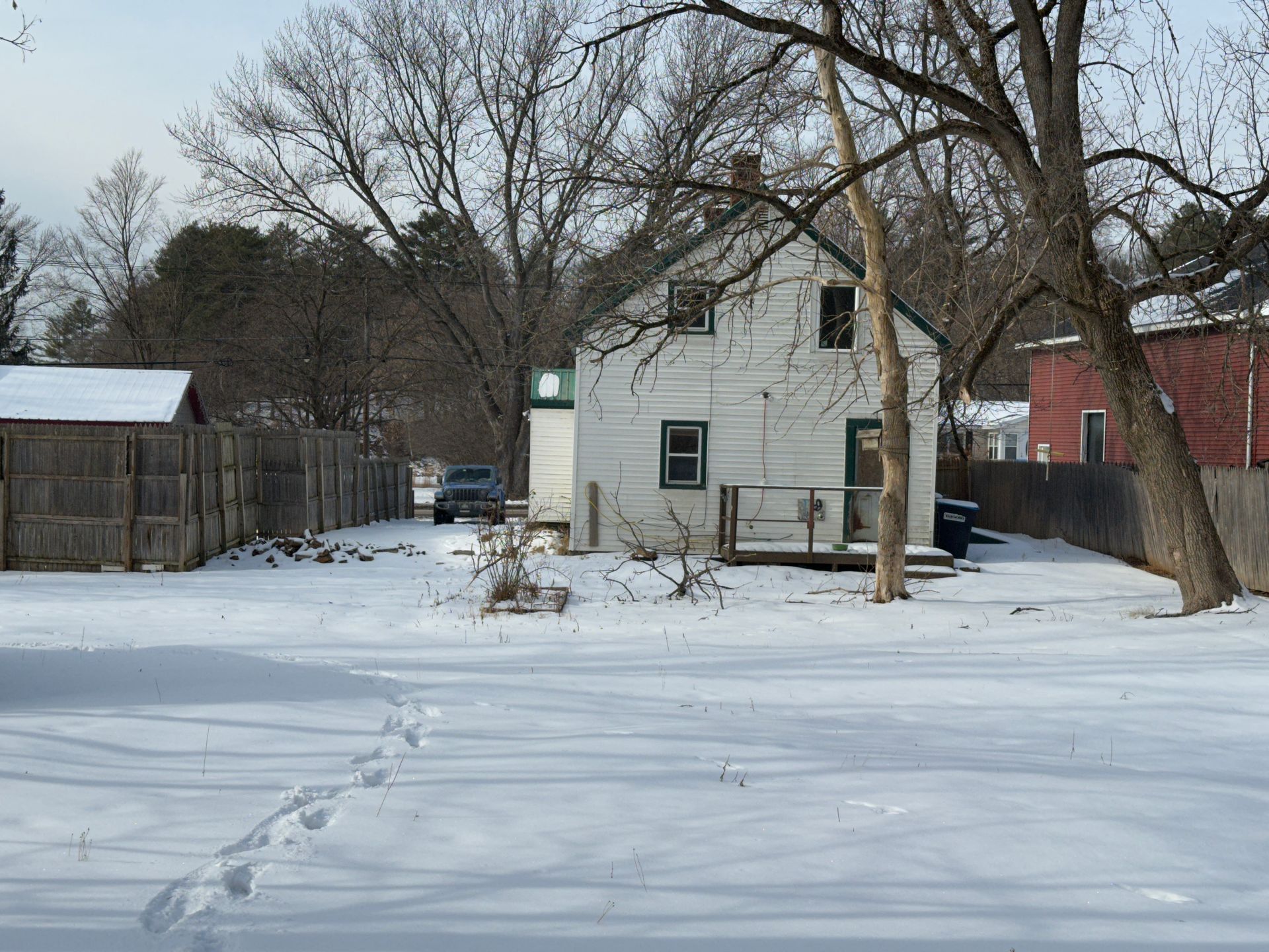 Snow-covered yard with a two-story white house and a wooden fence; a car parked in the driveway.