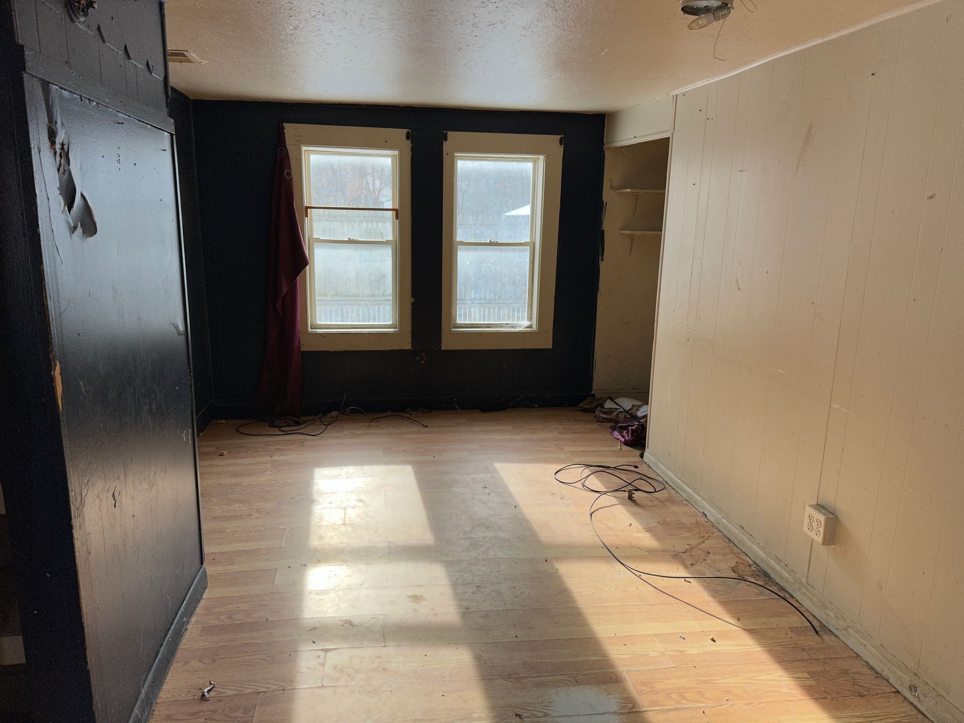 Empty room with two windows, dark walls, and flooring. Sunlight streams in.