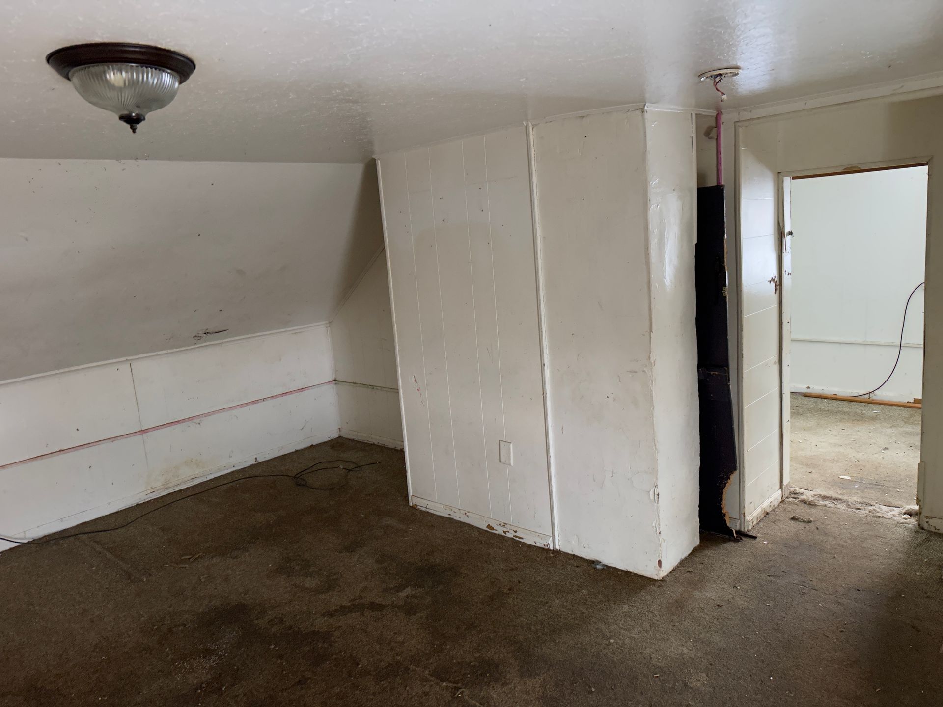 Room with angled walls, floor, white paneling, door to another room.