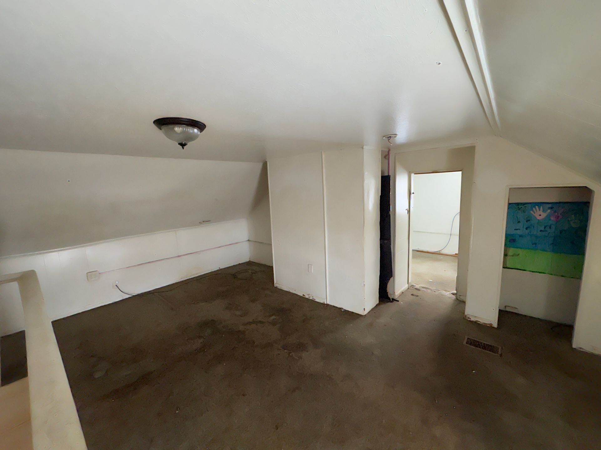 Room with slanted ceilings, white walls, dark floor, and an open doorway.