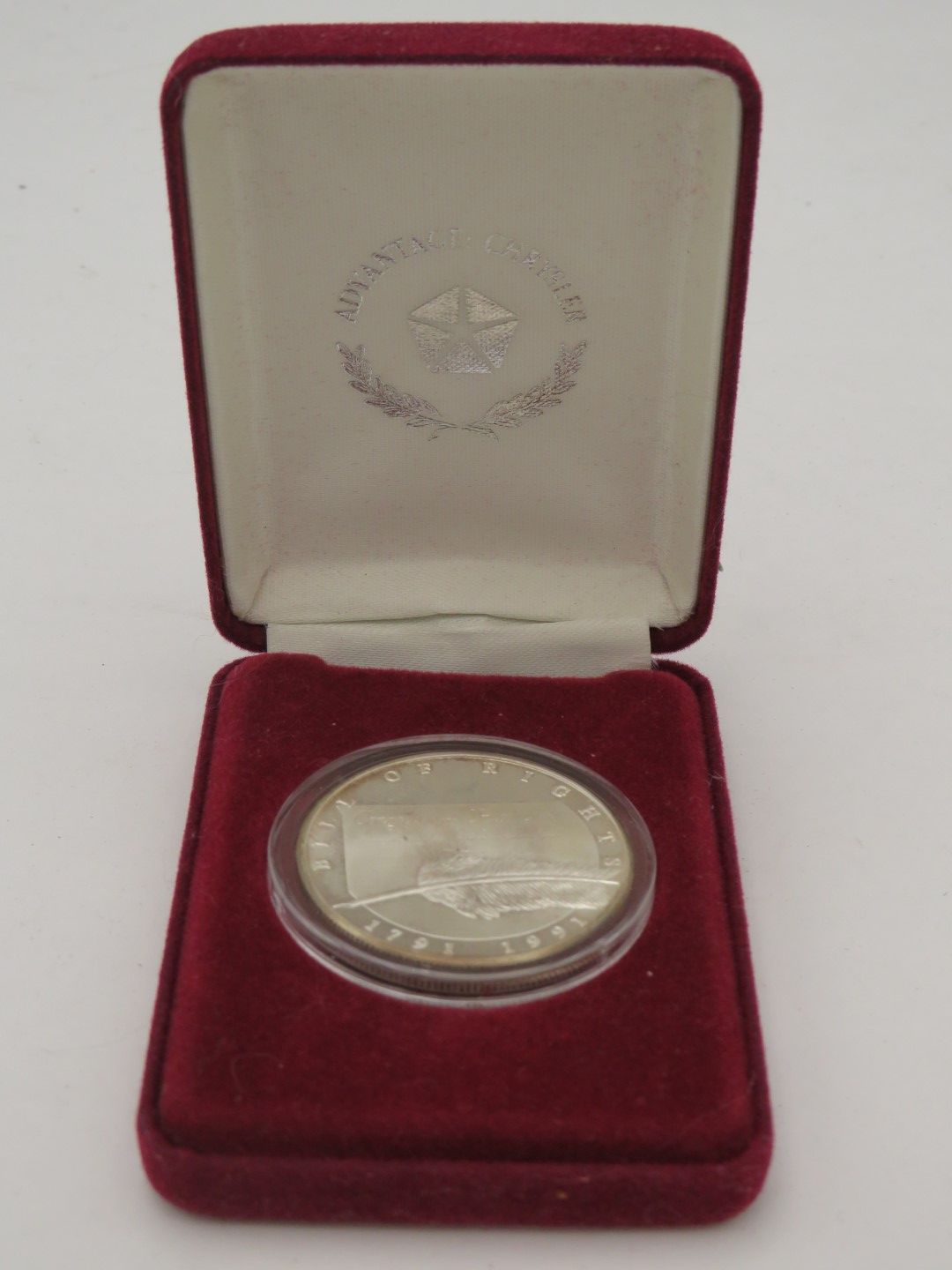 A silver coin in a clear case inside a red velvet box. The box is open, displaying the coin.