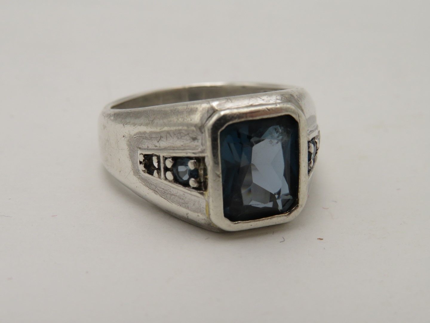 Silver ring with a large rectangular blue gemstone and smaller surrounding dark stones.