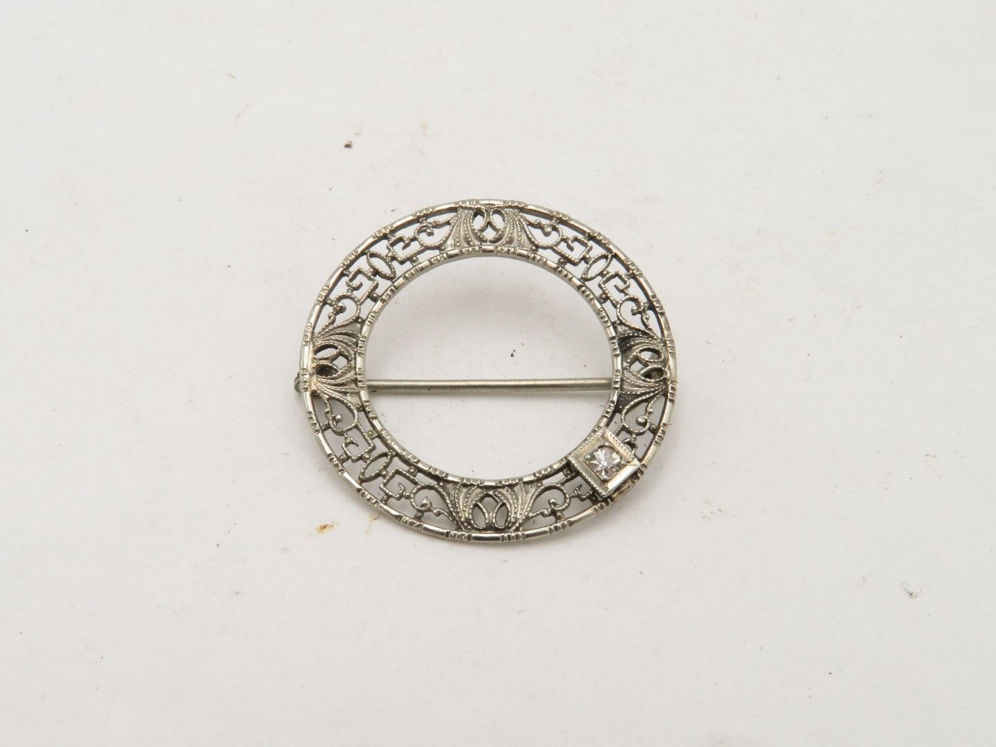 Silver filigree circle brooch with small diamonds and pin closure.