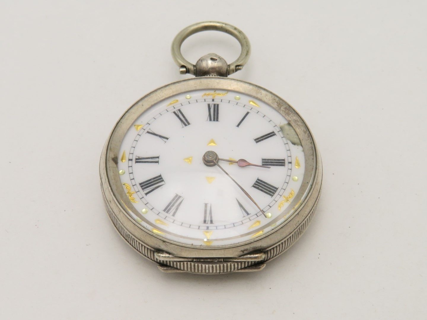 Silver pocket watch with white face, black Roman numerals, gold accents.