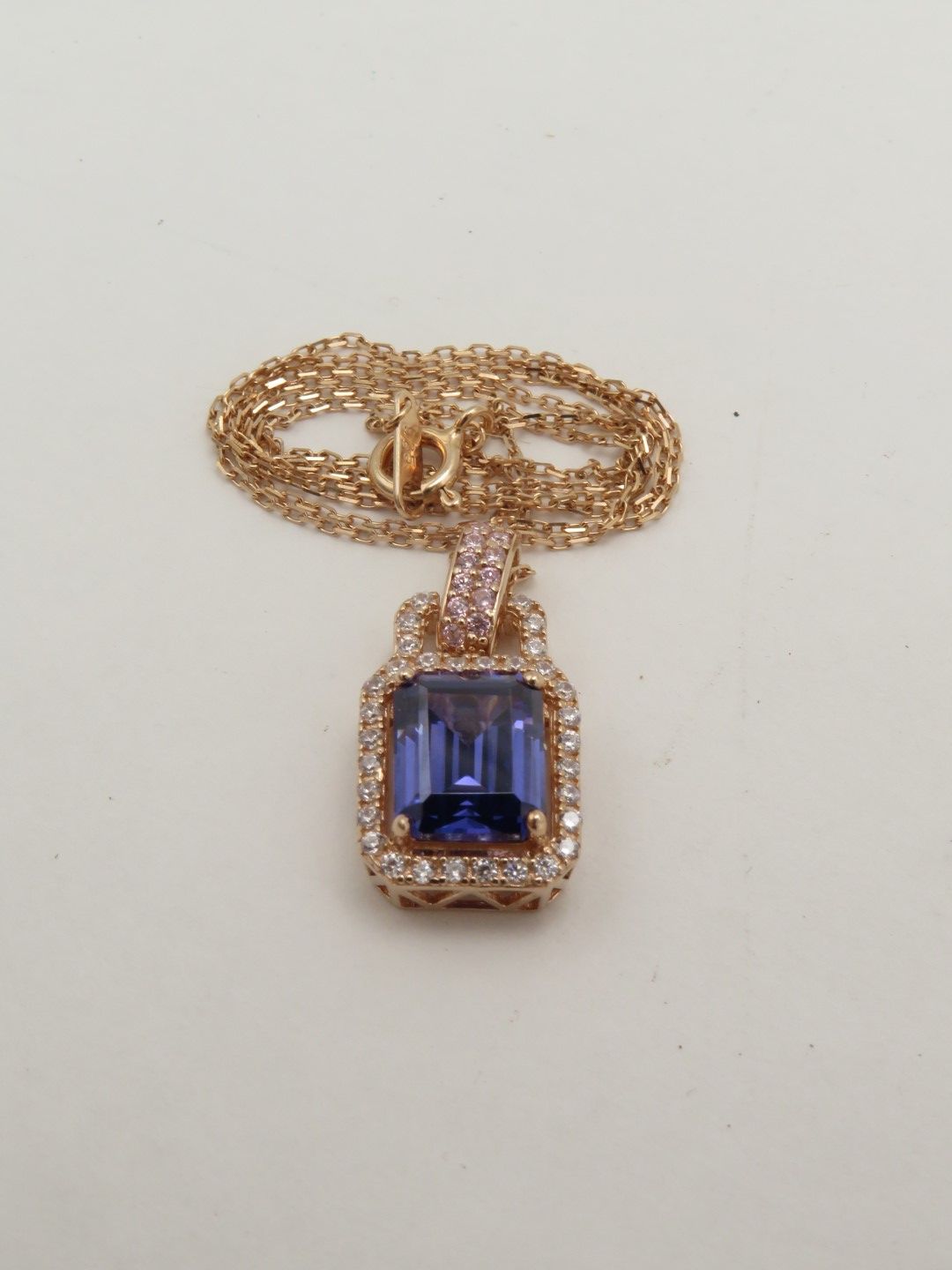 Rose gold necklace with a rectangular blue gemstone pendant and surrounding diamonds.