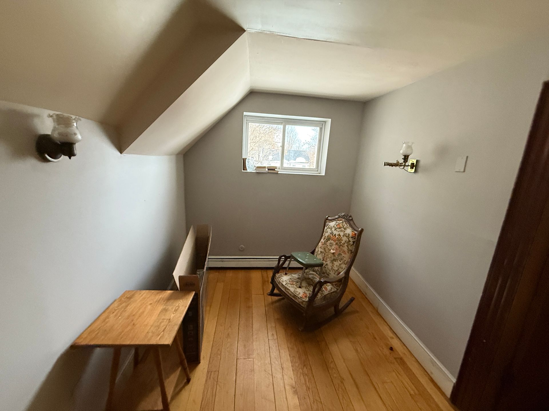 Small room with sloped ceiling, window, wooden floor, and a rocking chair.