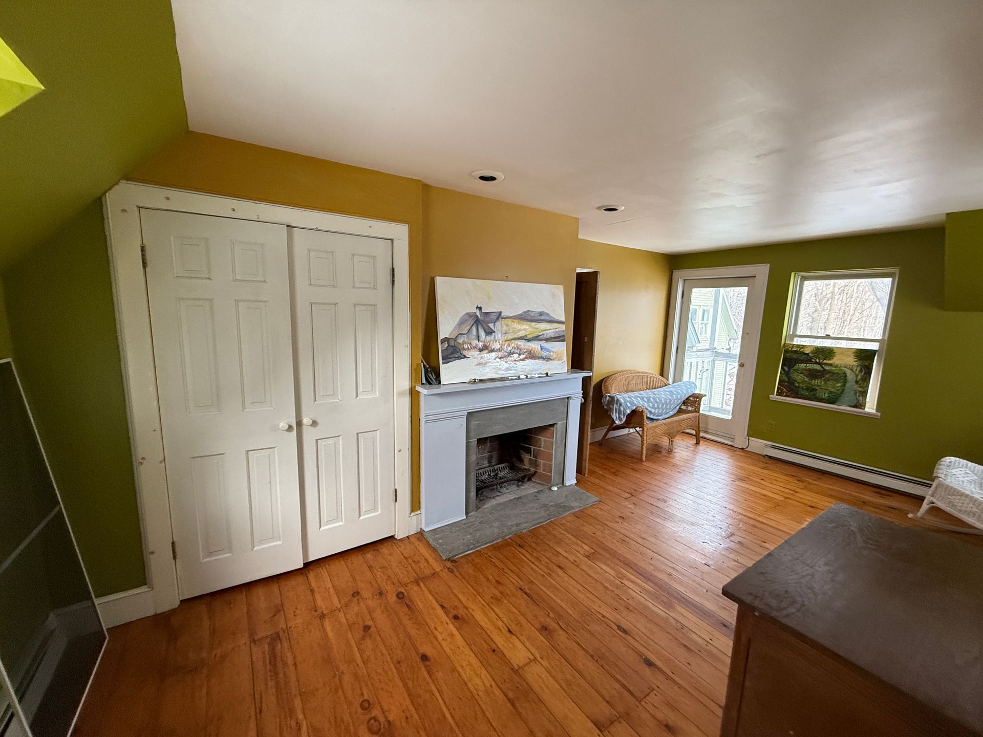 Bedroom with hardwood floors, closet, fireplace, and a door leading outside. Green and gold walls, natural light.