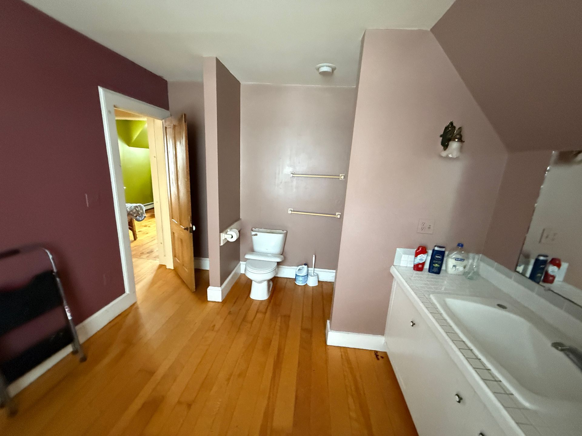 Bathroom with hardwood floors, toilet, sink, and open door to another room. Walls are shades of mauve.