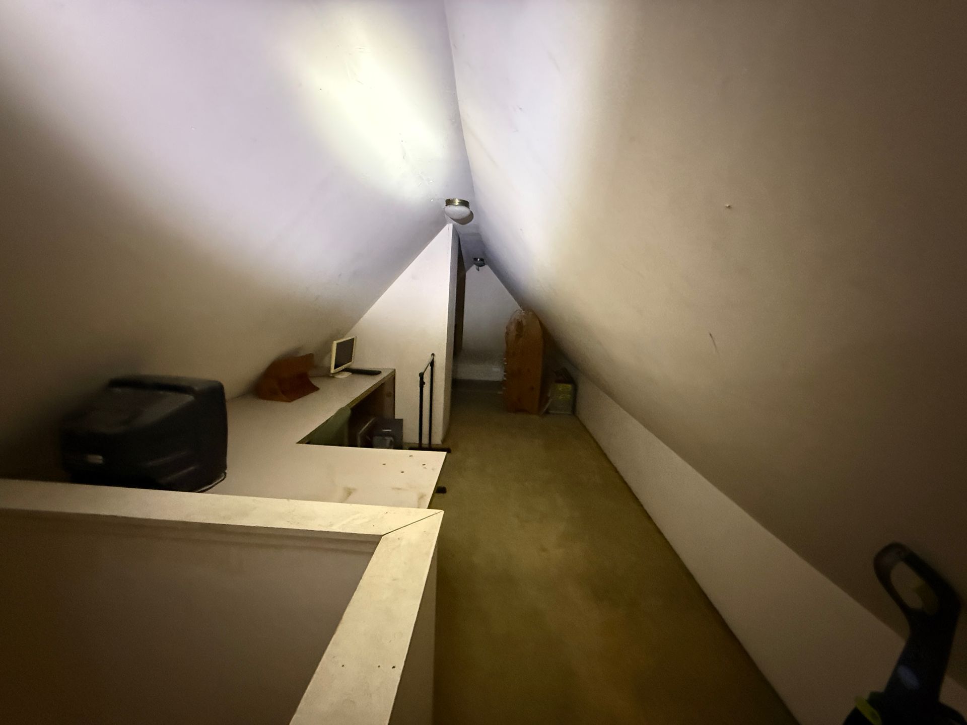 Attic space with angled ceilings, built-in desk, and light source.