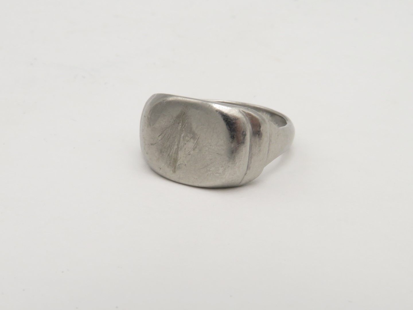 Silver signet ring on a white background, featuring a square face with etched design.