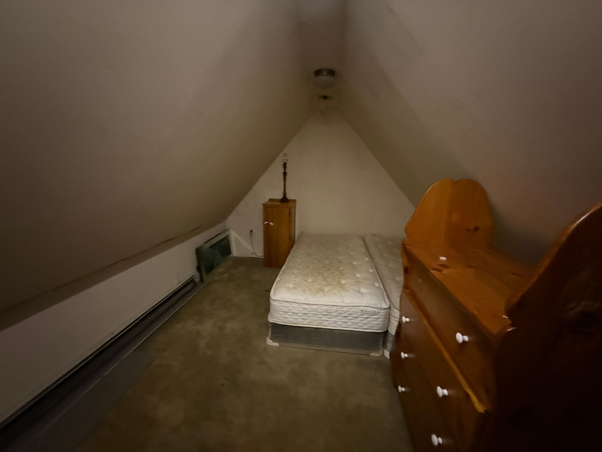 Attic bedroom with bed, dresser, and guitar leaning against the wall.