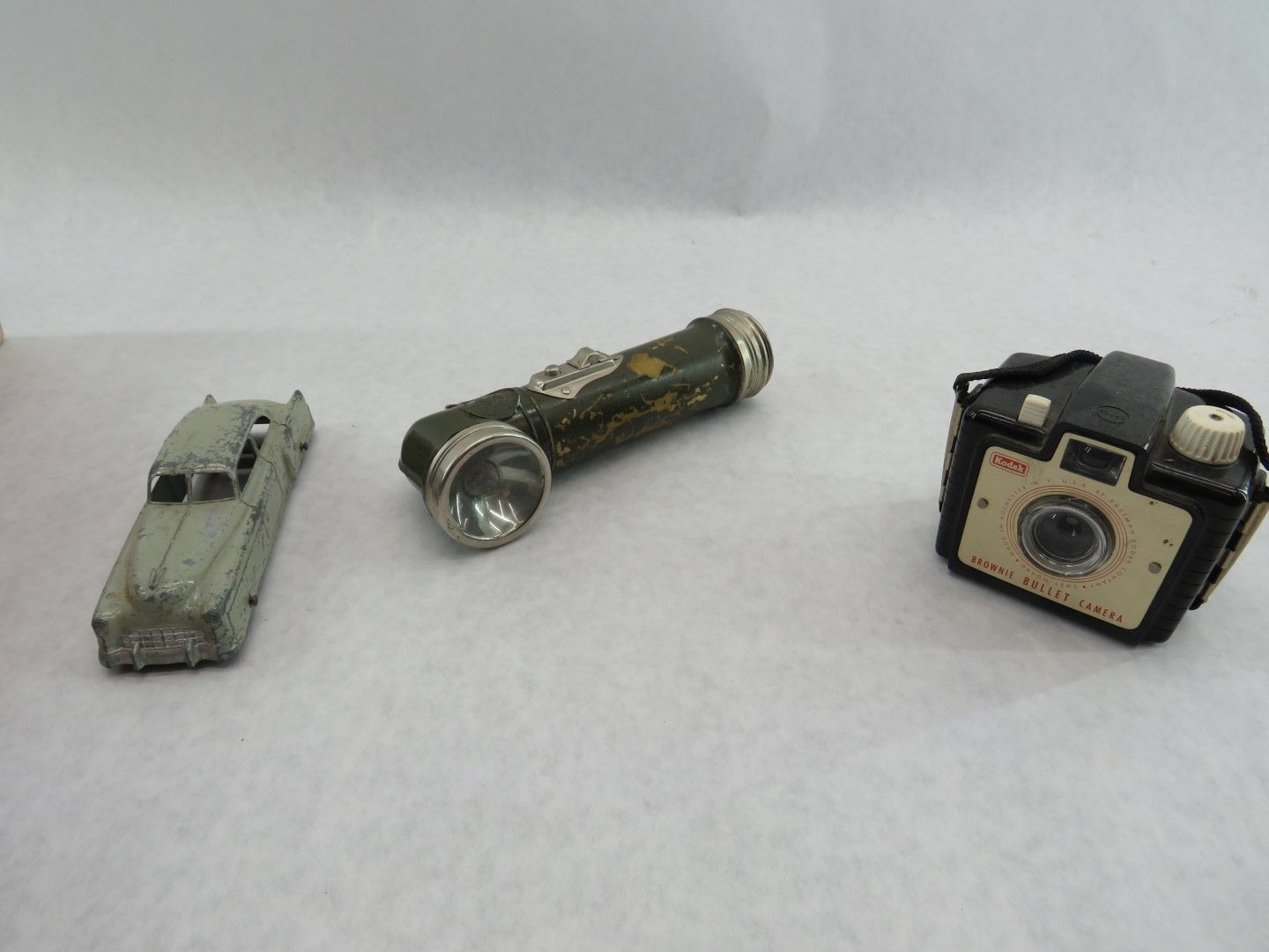 Toy car, flashlight, and camera on a white surface. Antique.