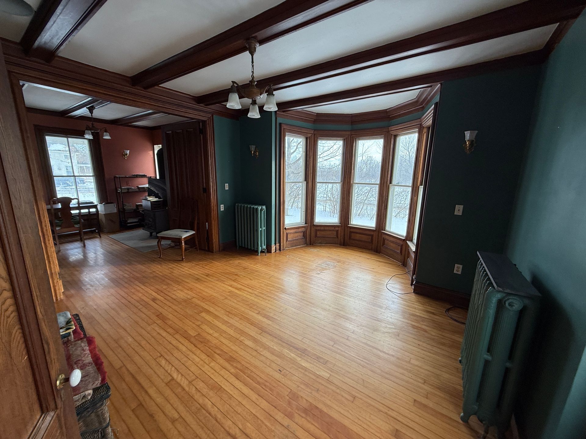 Wooden-floored room with a bay window, exposed beams, and a radiator. Dark green and wood accents.