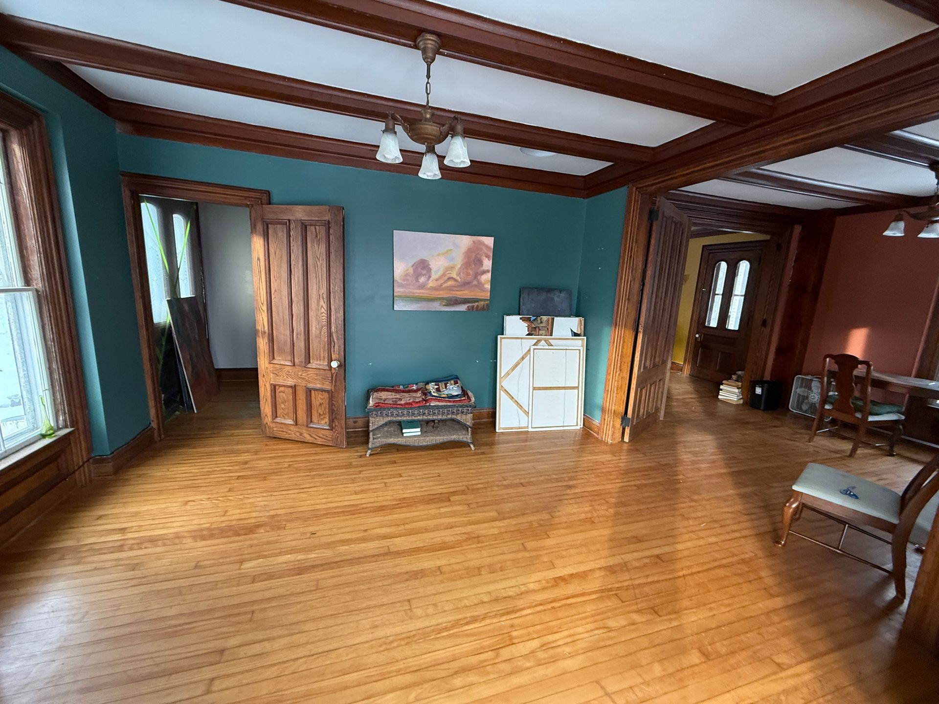 Wooden-floored room with teal walls, dark wooden trim, a painting, and an open doorway.